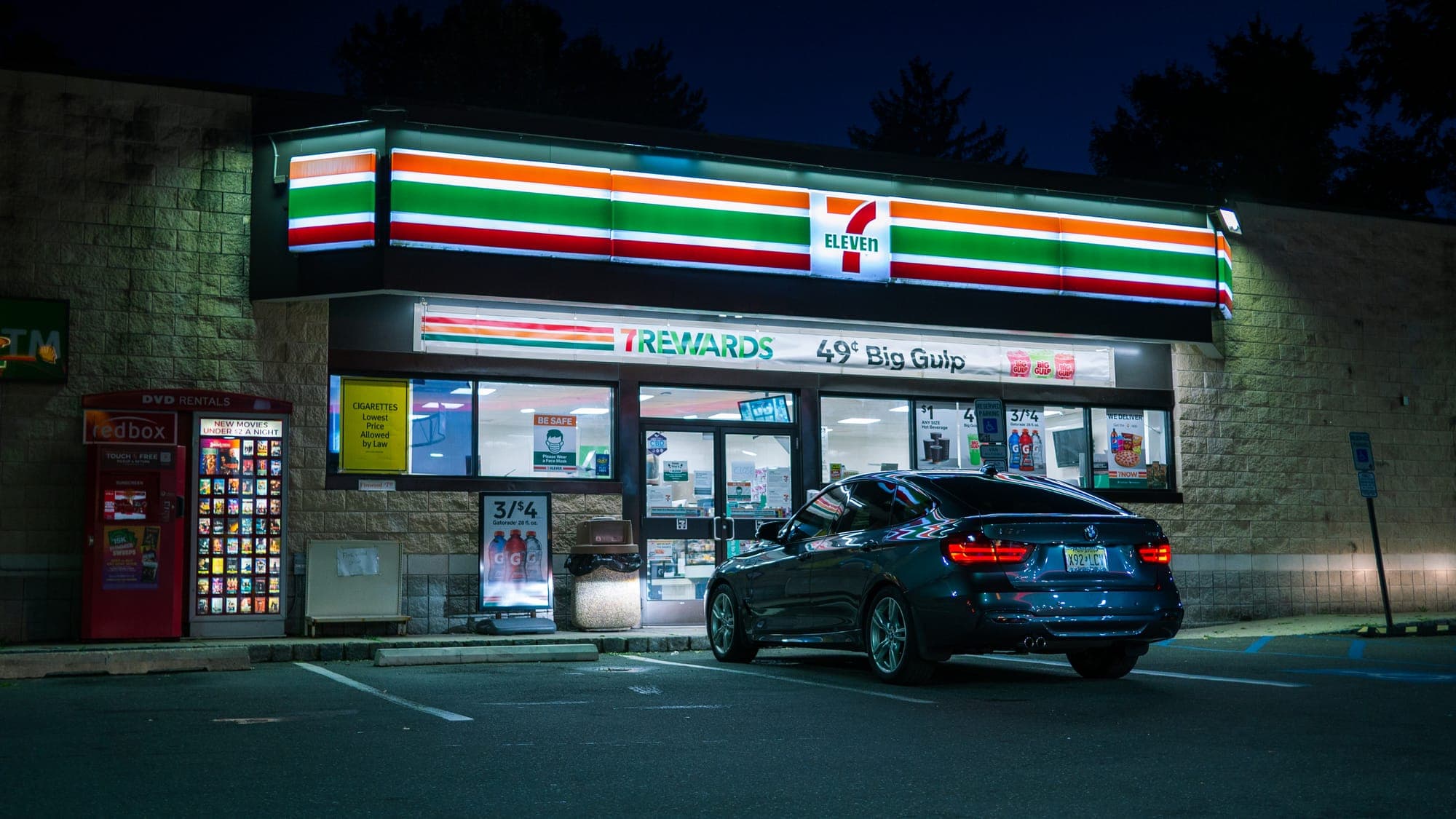 Dark blue BMW 3 Series GT parked outside a glowing convenience-store front at night.