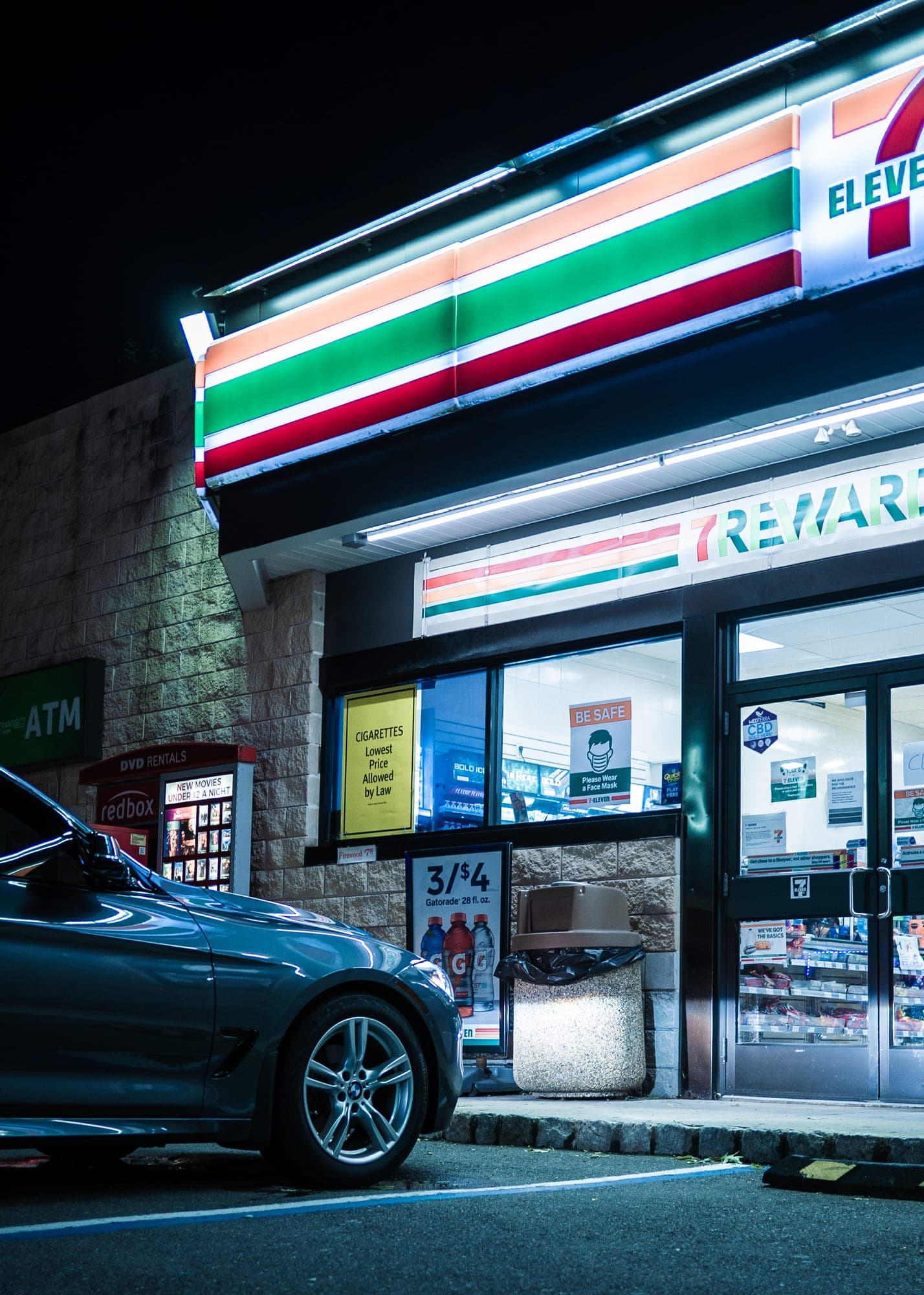 Front fender and wheel of a blue BMW under fluorescent storefront light at night.