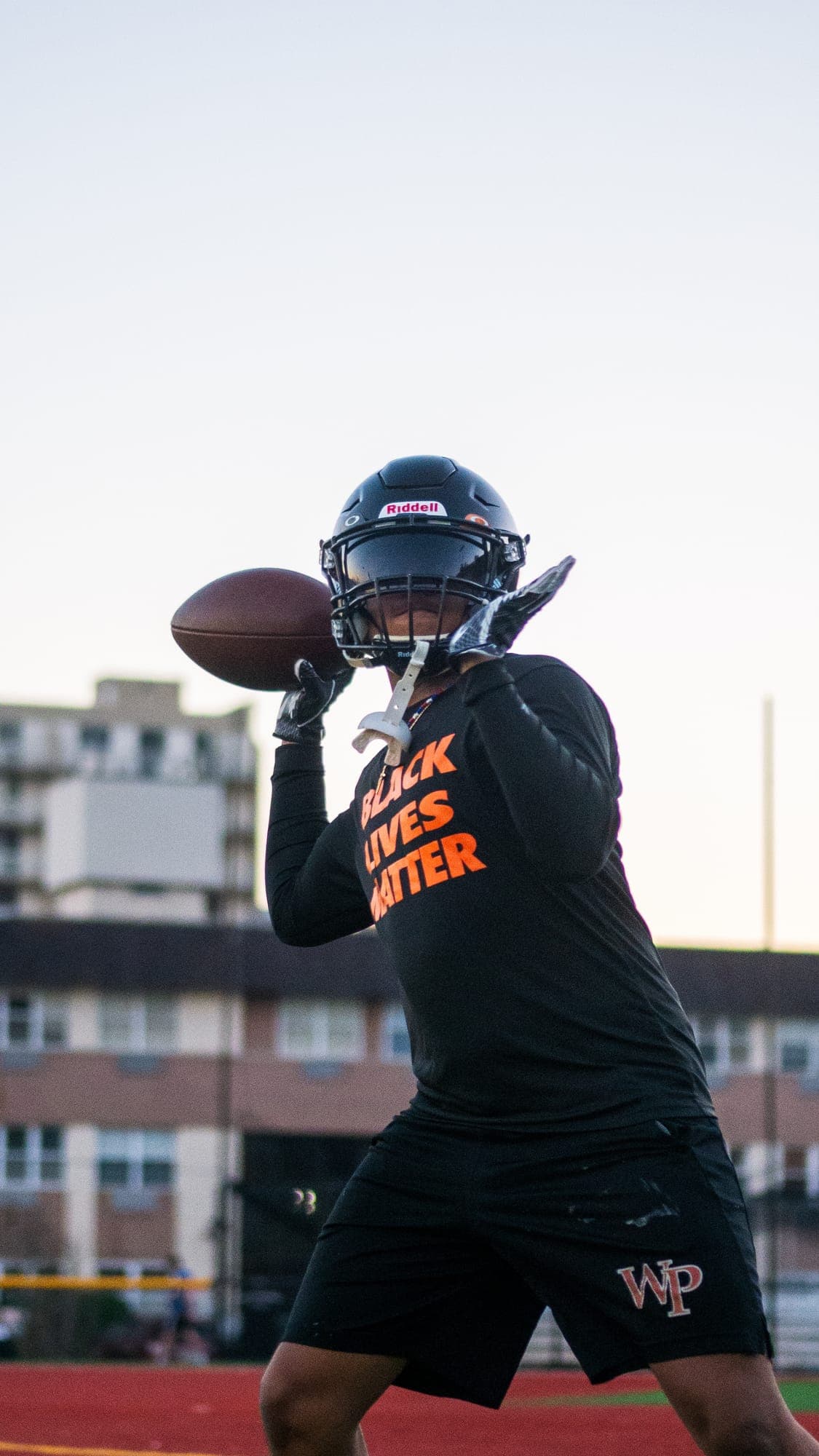 Football player drawing the ball back behind his helmet to pass, city buildings soft in the background