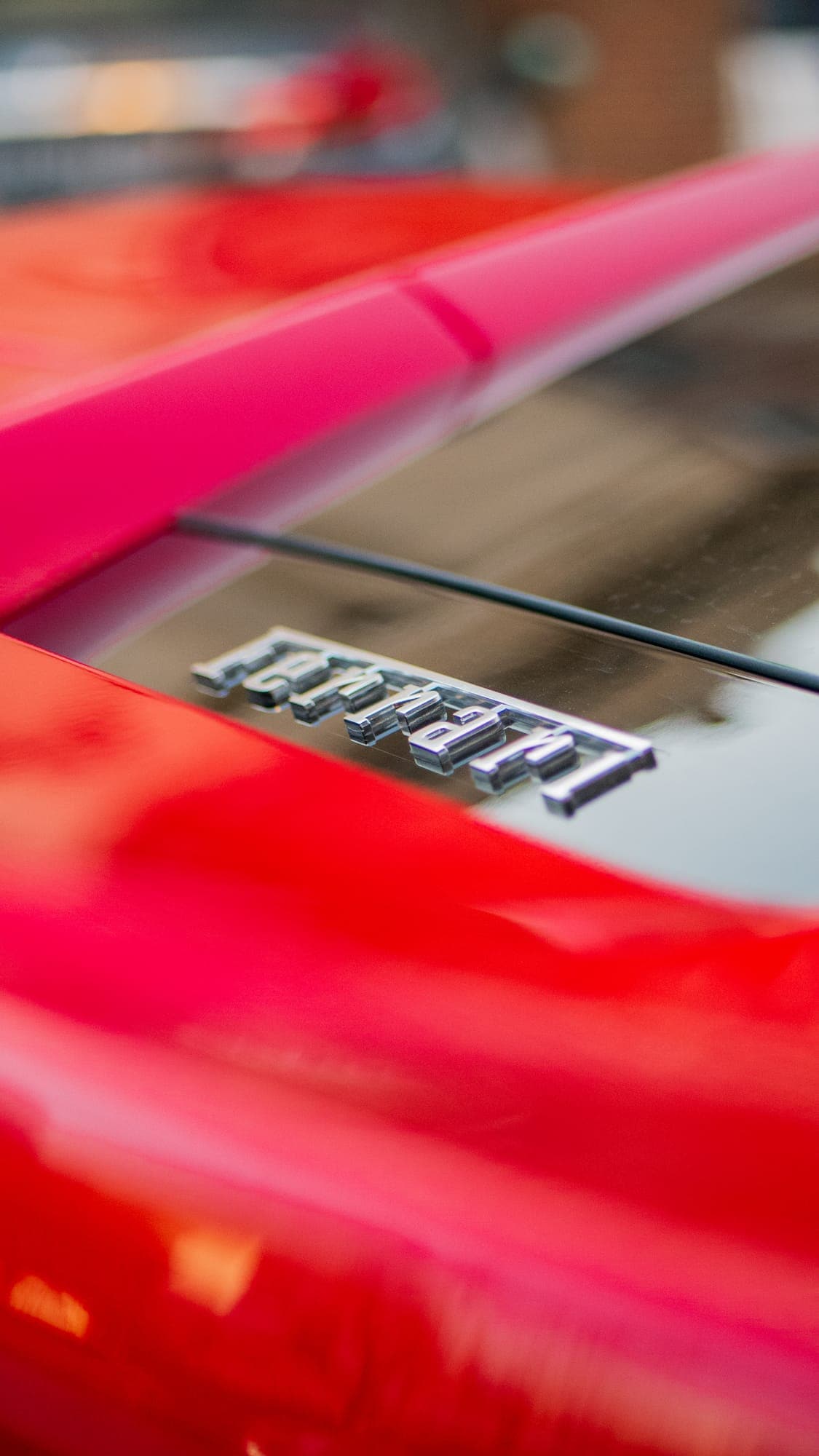 Chrome Ferrari script badge on the red decklid of a 488, in shallow depth of field.