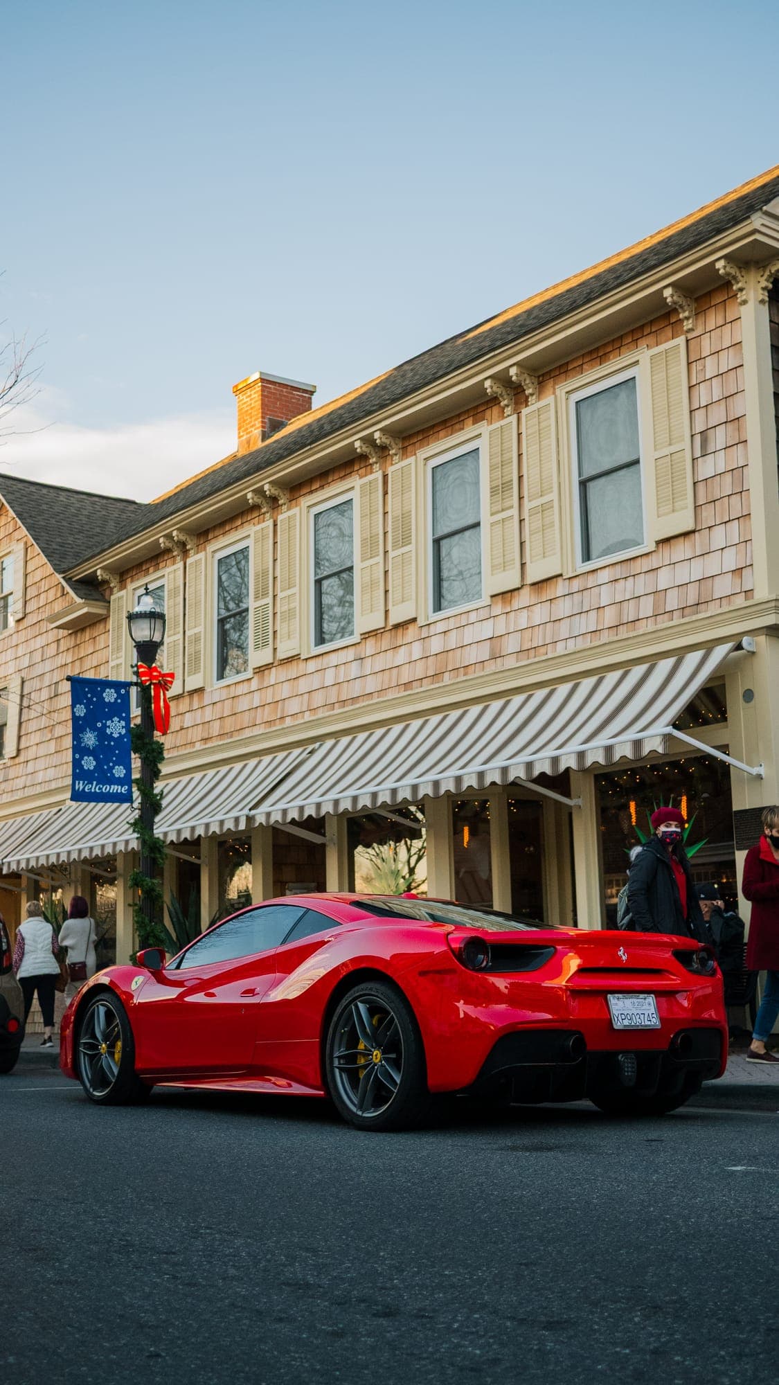 Red Ferrari 488 GTB from the rear three-quarter, parked on a small-town main street dressed with holiday decorations.
