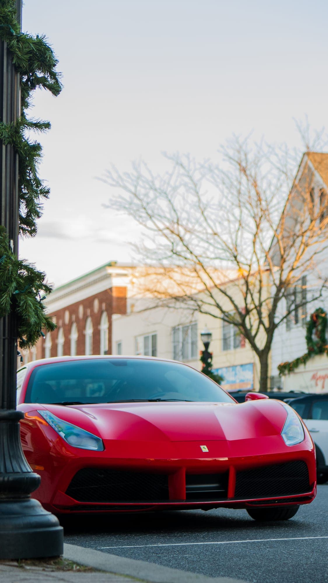 Red Ferrari 488 GTB nose framed past a garlanded lamppost on a winter main street.