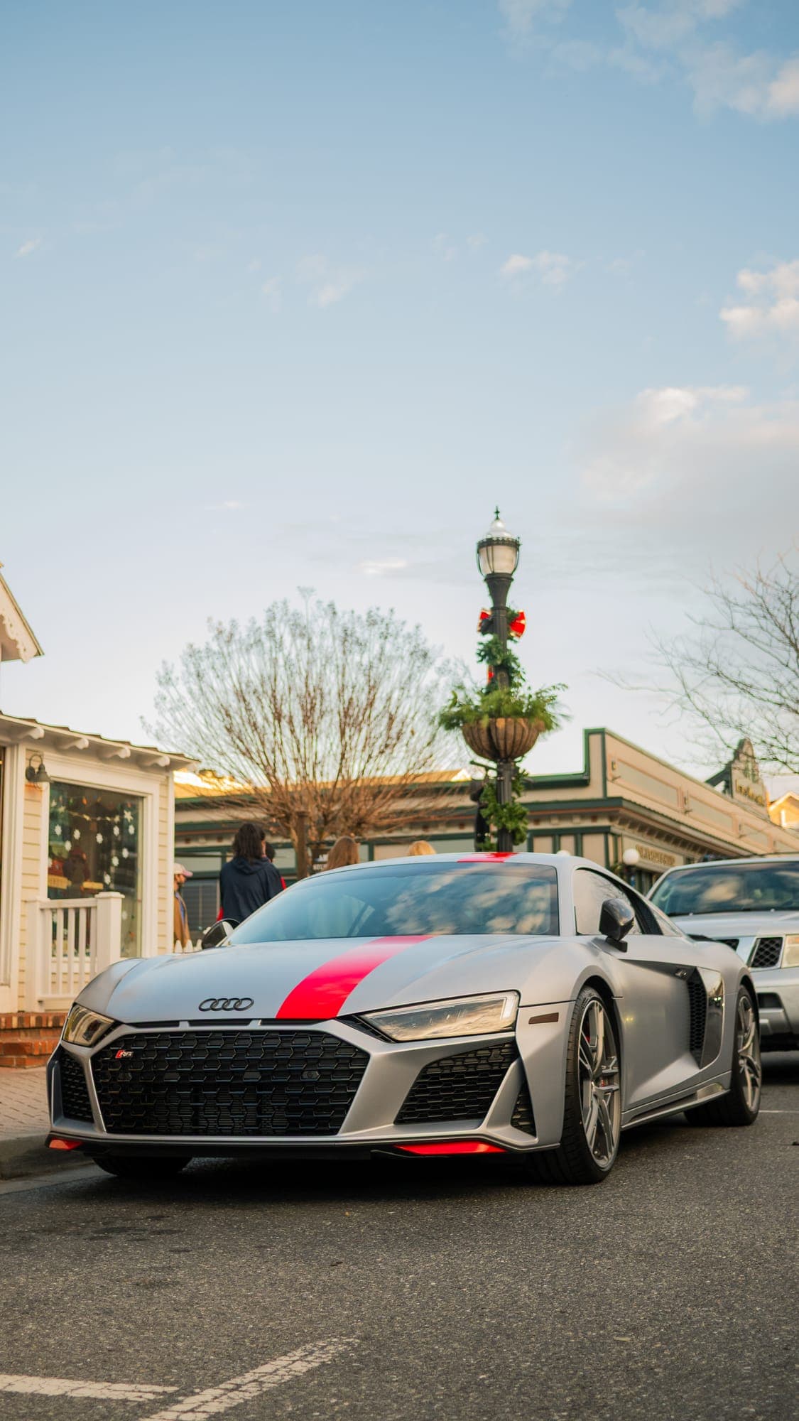 Silver Audi R8 front three-quarter beneath a wreathed lamppost at golden hour.