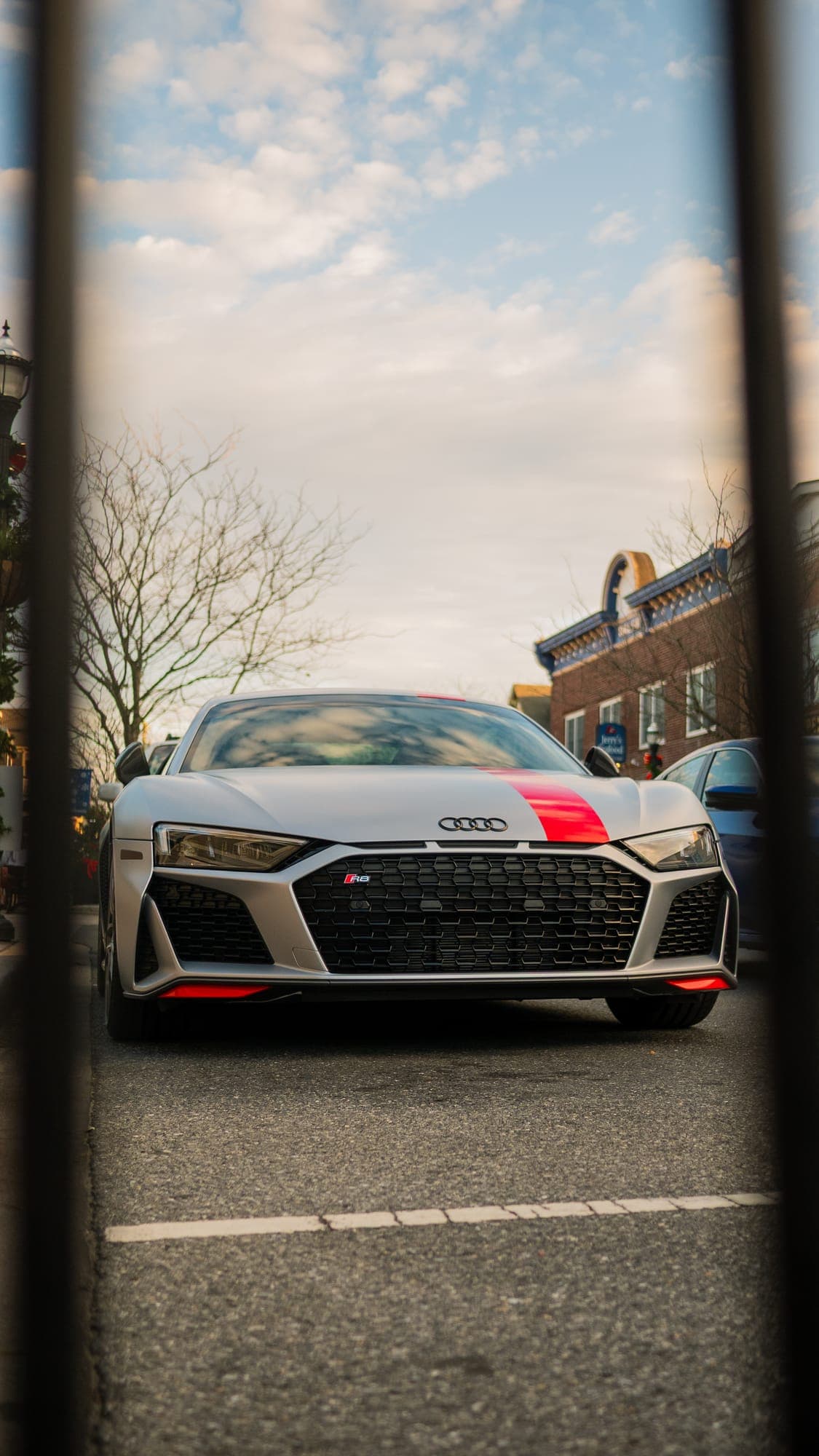 Silver Audi R8 grille head-on, framed between dark posts across the street.