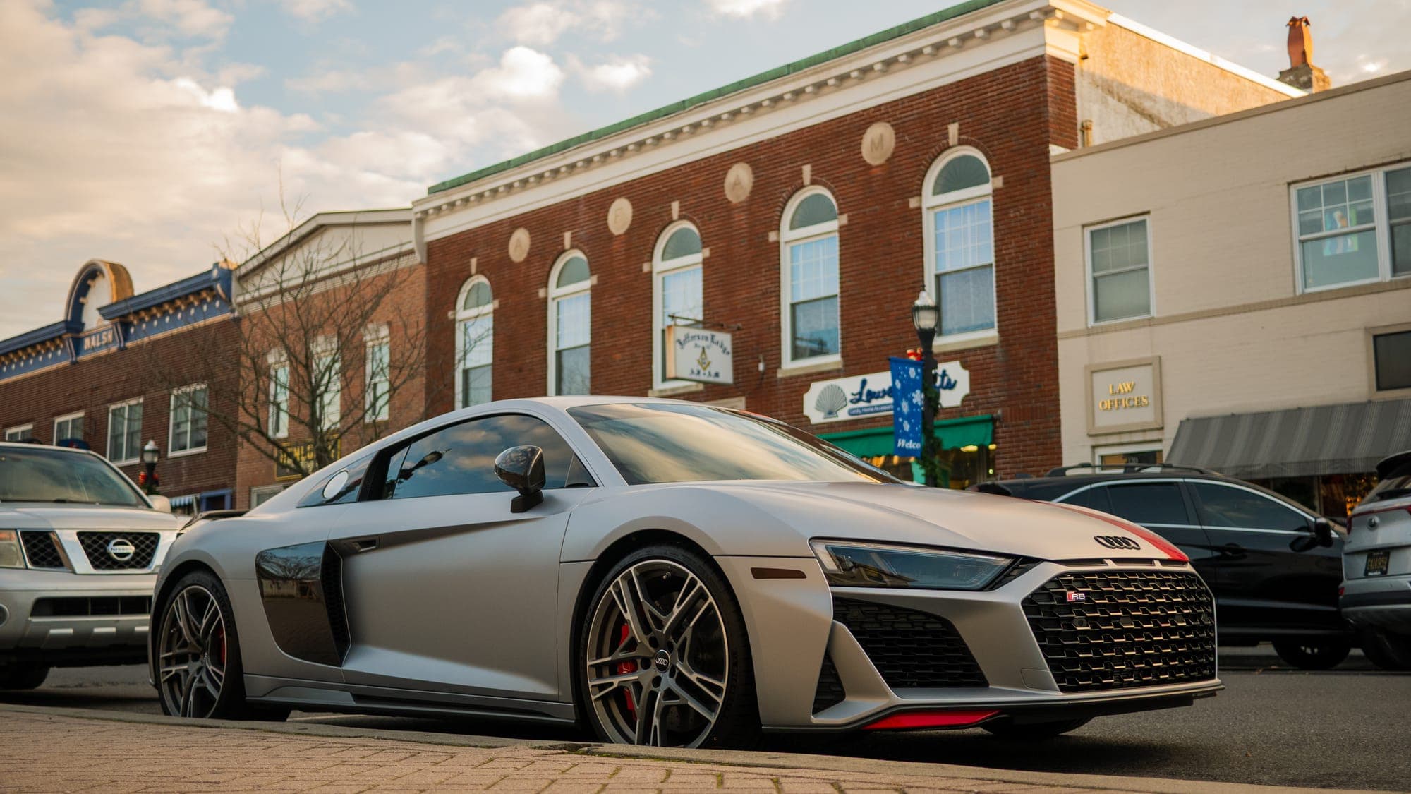 Matte gray Audi R8 with red accents parked on a small-town main street in golden evening light.