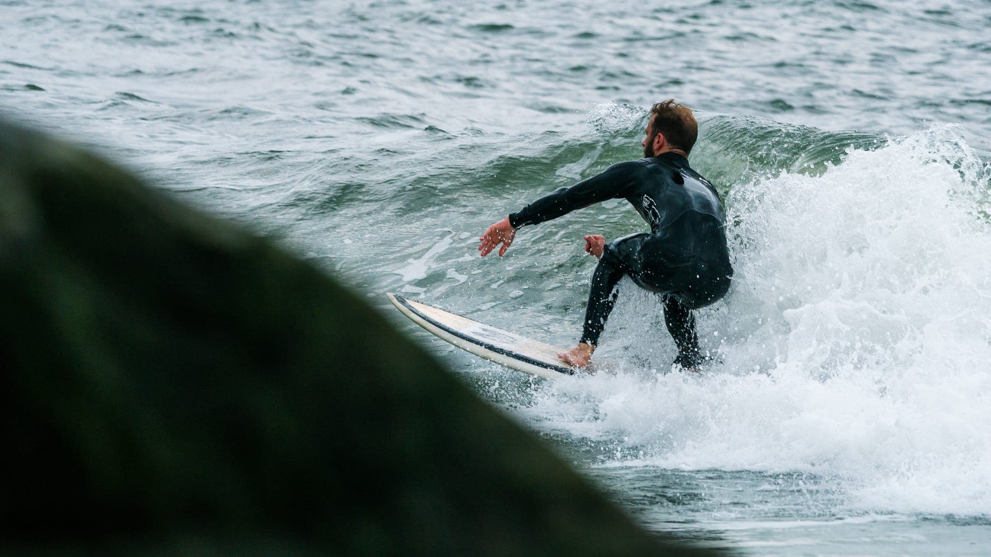 Surfer carving a turn through whitewater, arms spread and board tail buried in foam