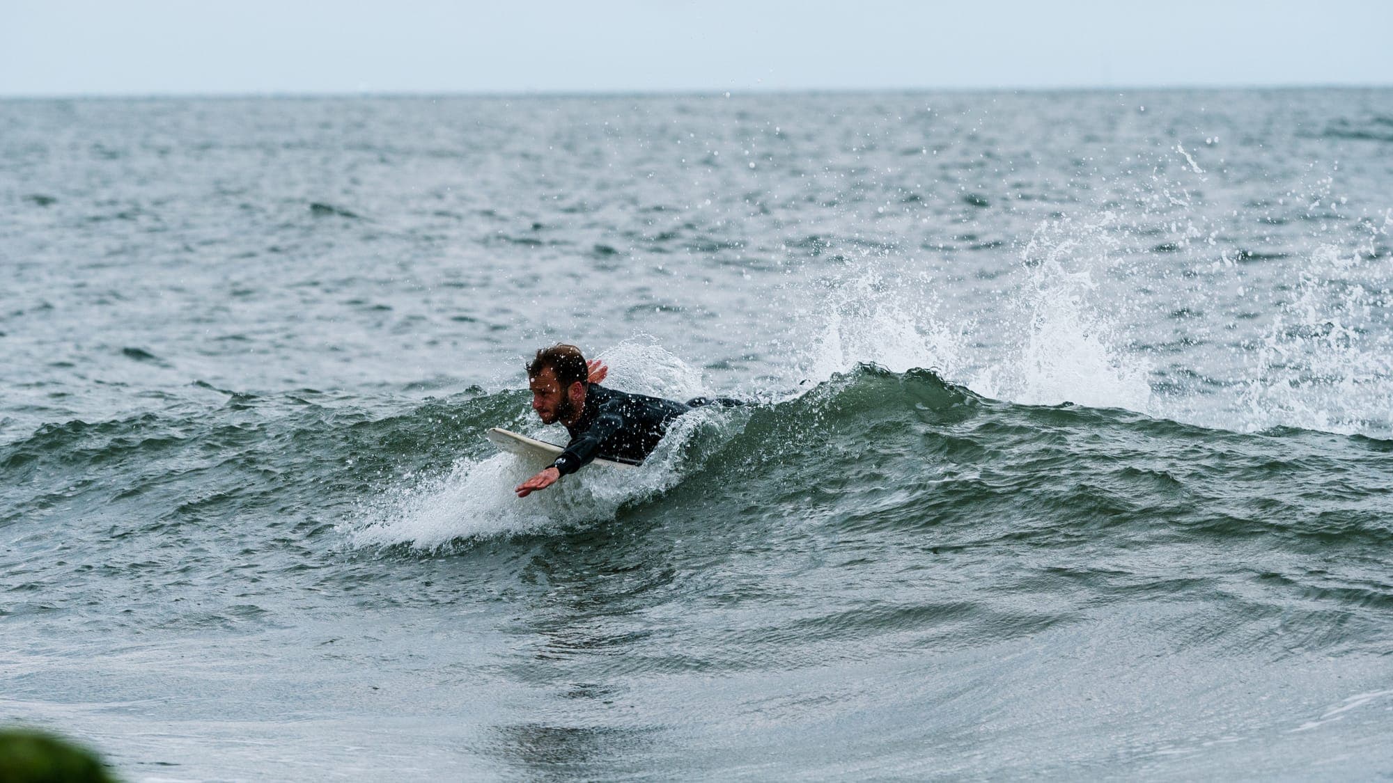 Surfer mid pop-up on a small green wave, spray trailing across the open ocean