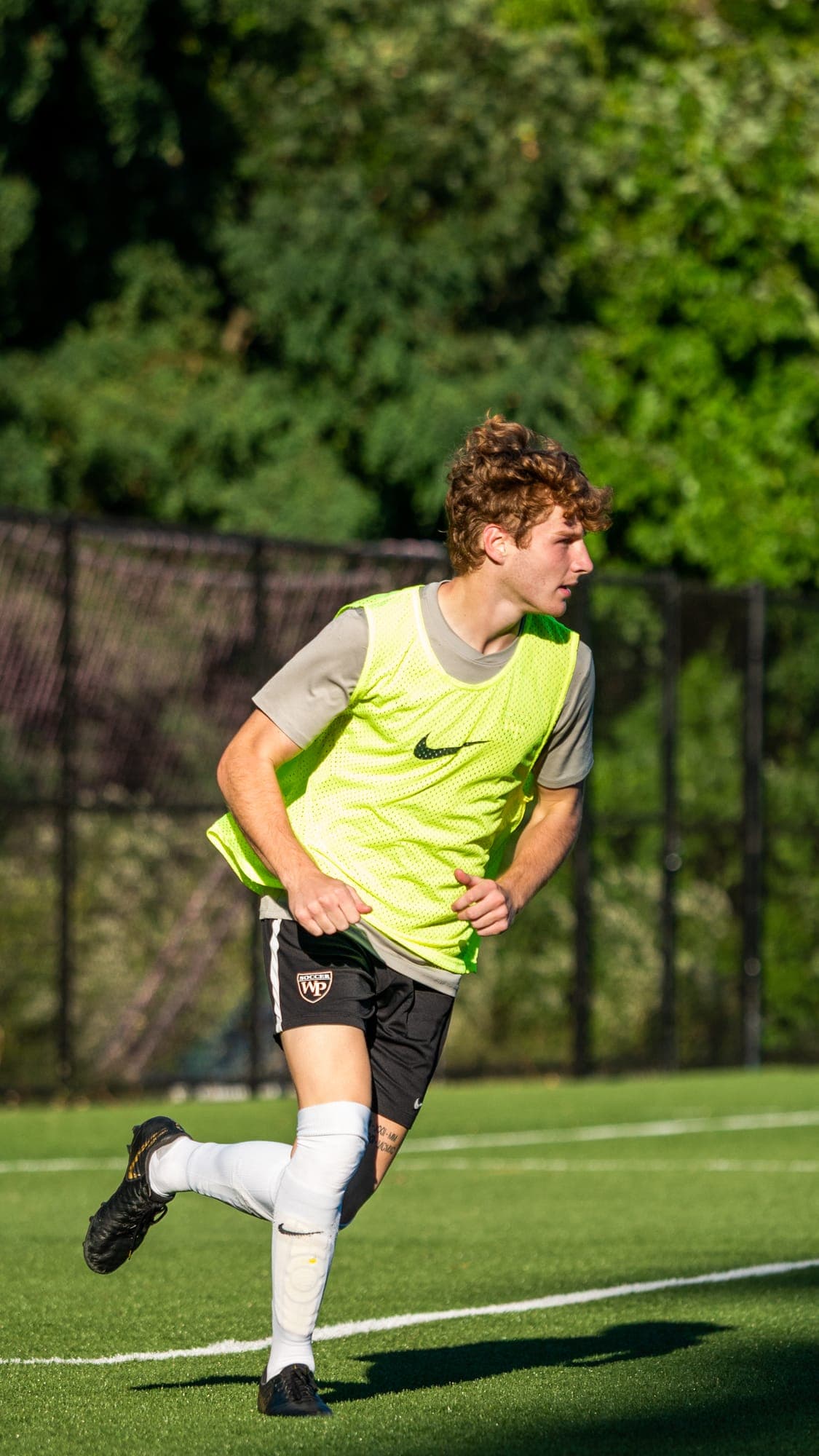 Soccer player in a yellow training bib jogging upfield, eyes tracking play off-frame