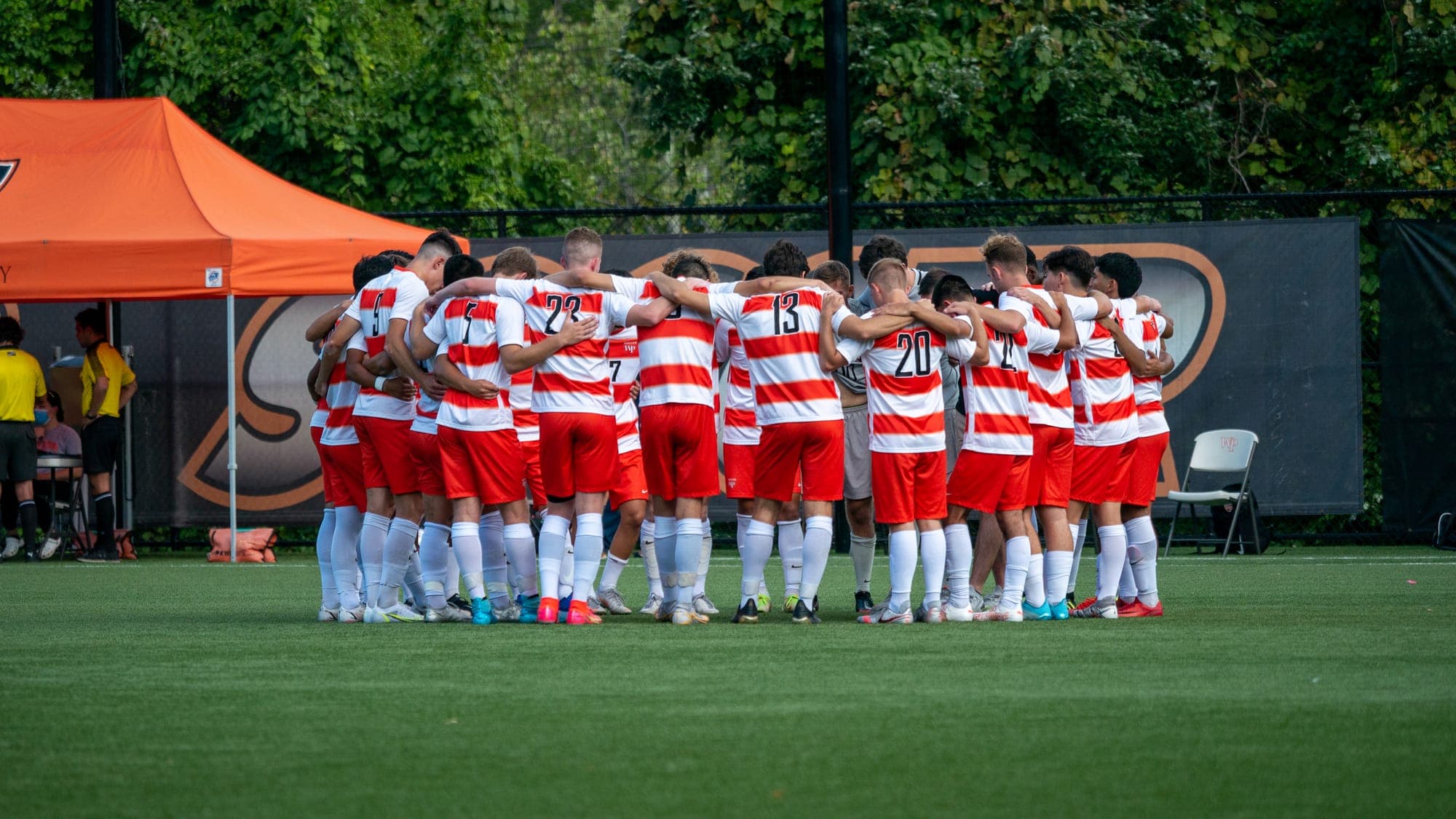Soccer team in red-and-white hooped kits huddled arm-in-arm on the pitch before kickoff