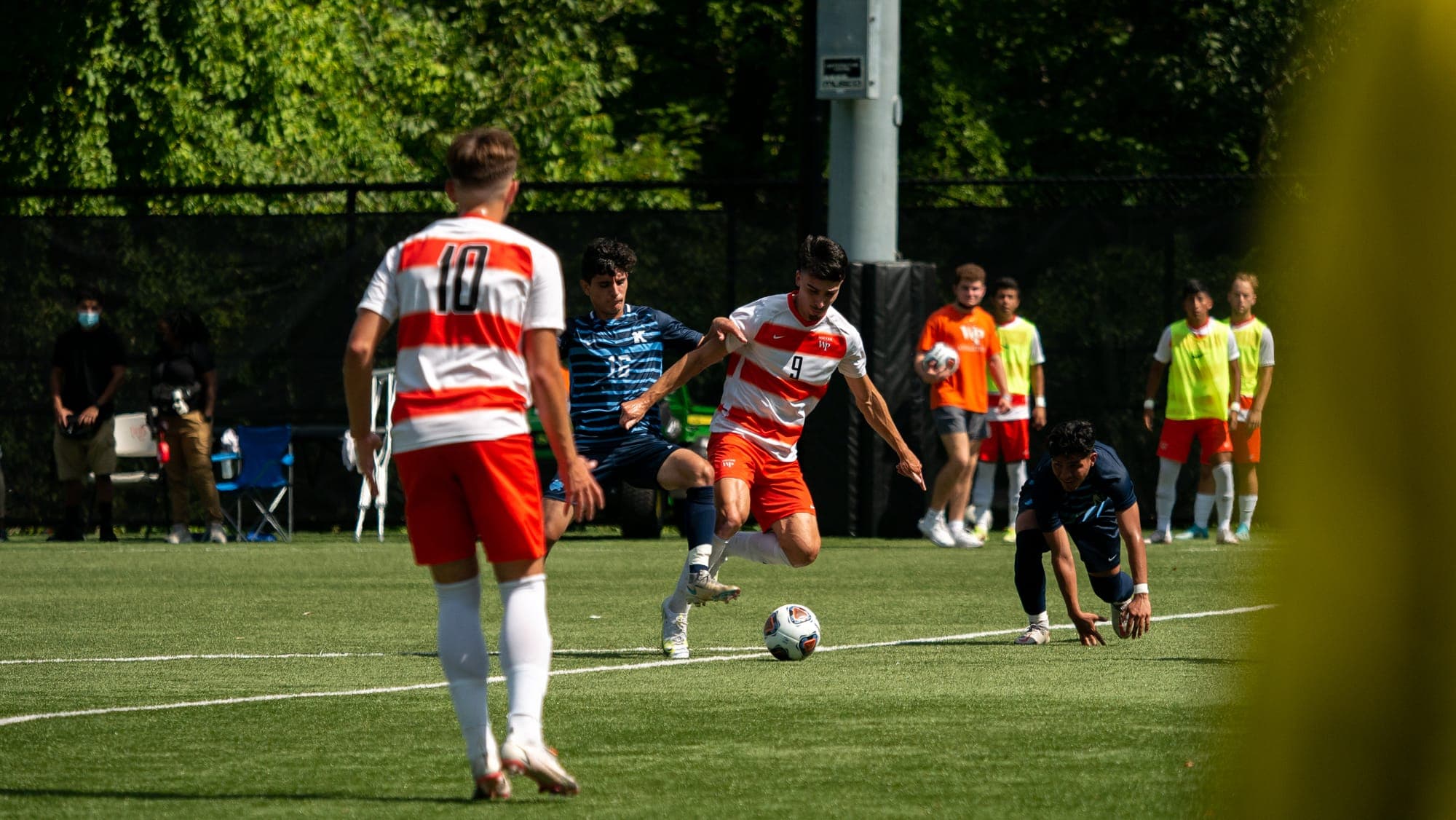 Soccer forward in hooped number 9 shirt driving the ball past a sliding defender in midfield