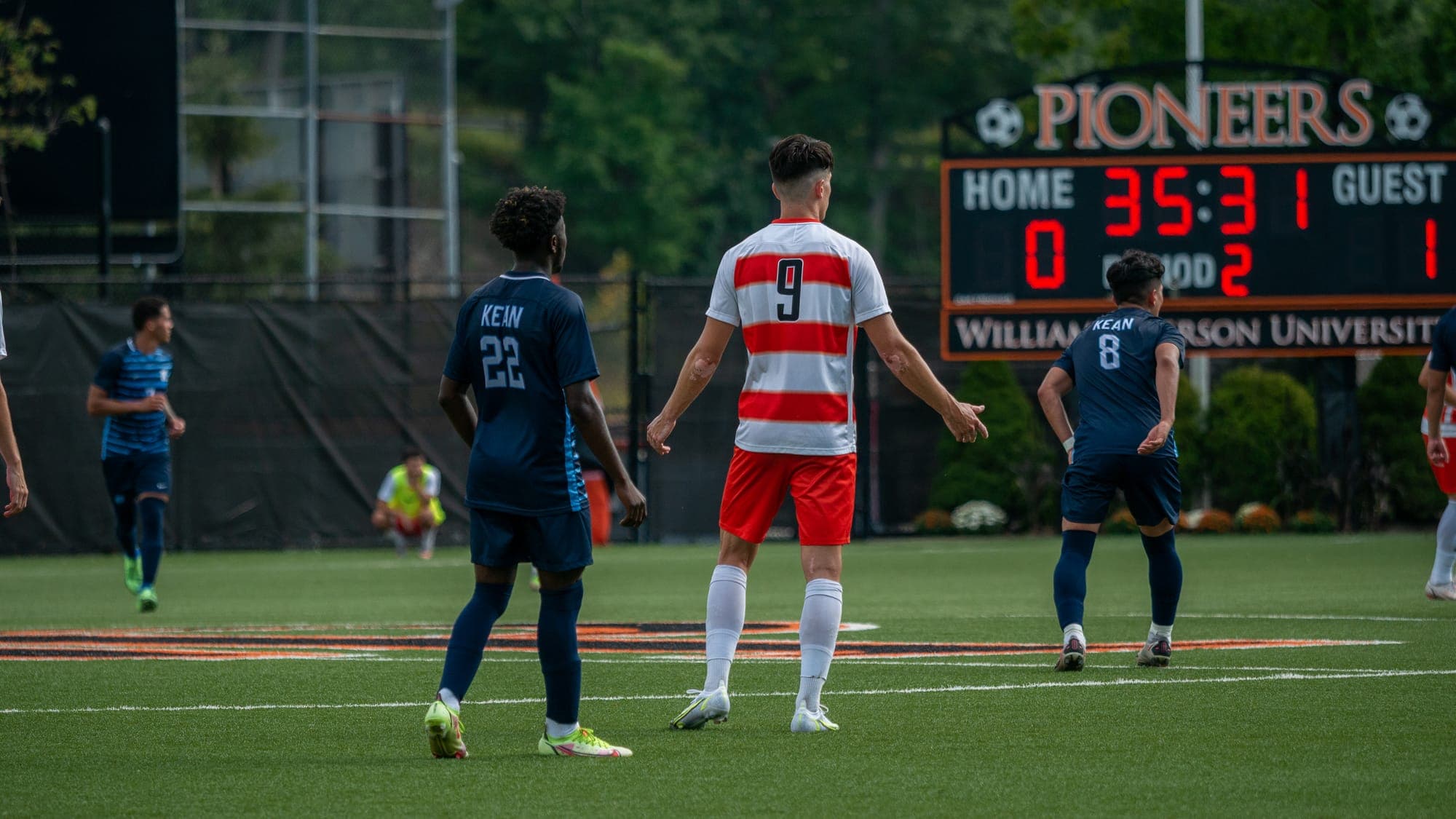 Players from both soccer teams reset on the pitch beneath the Pioneers scoreboard at William Paterson