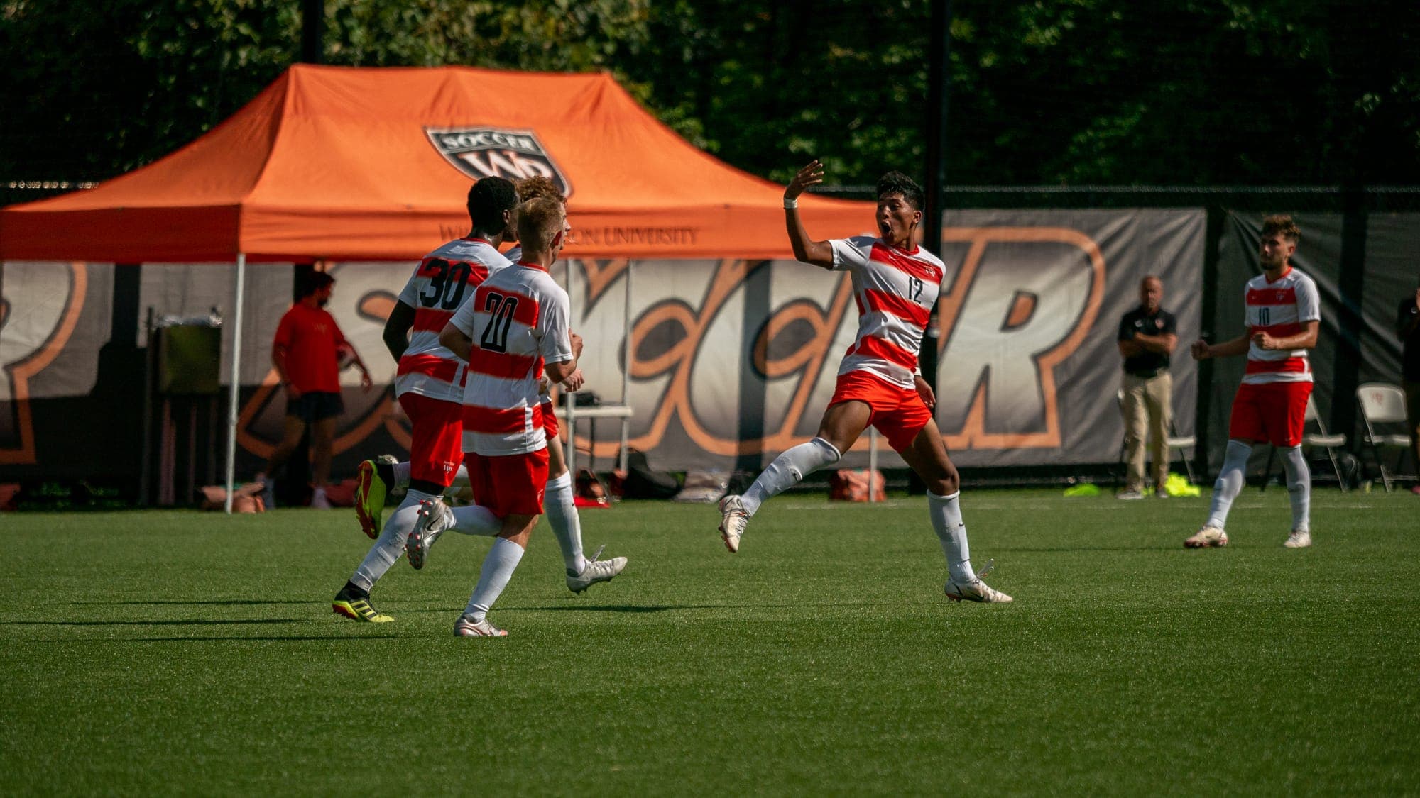 Soccer player leaping mid-air in celebration as teammates run toward him after a goal
