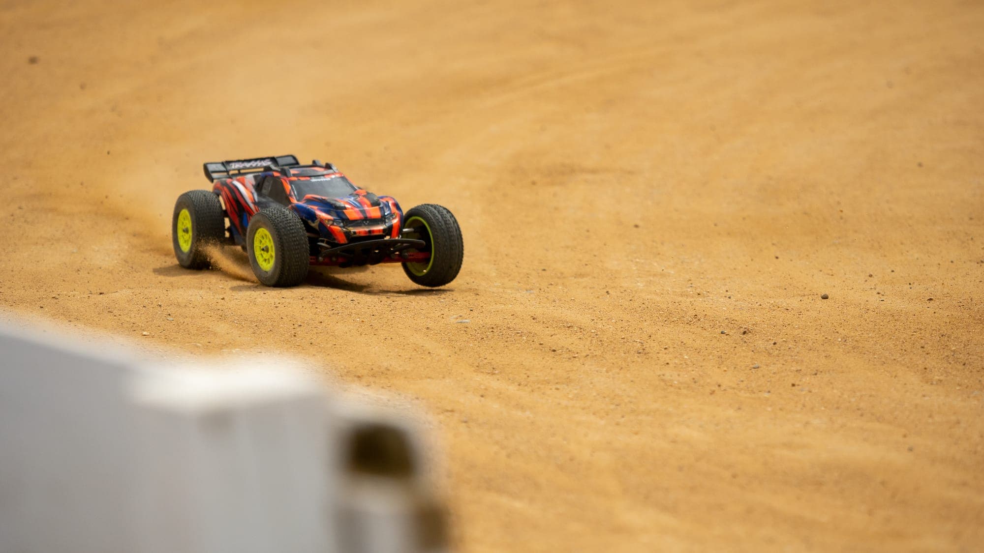 Traxxas RC truggy with yellow wheels charging across open dirt, dust trailing behind it.