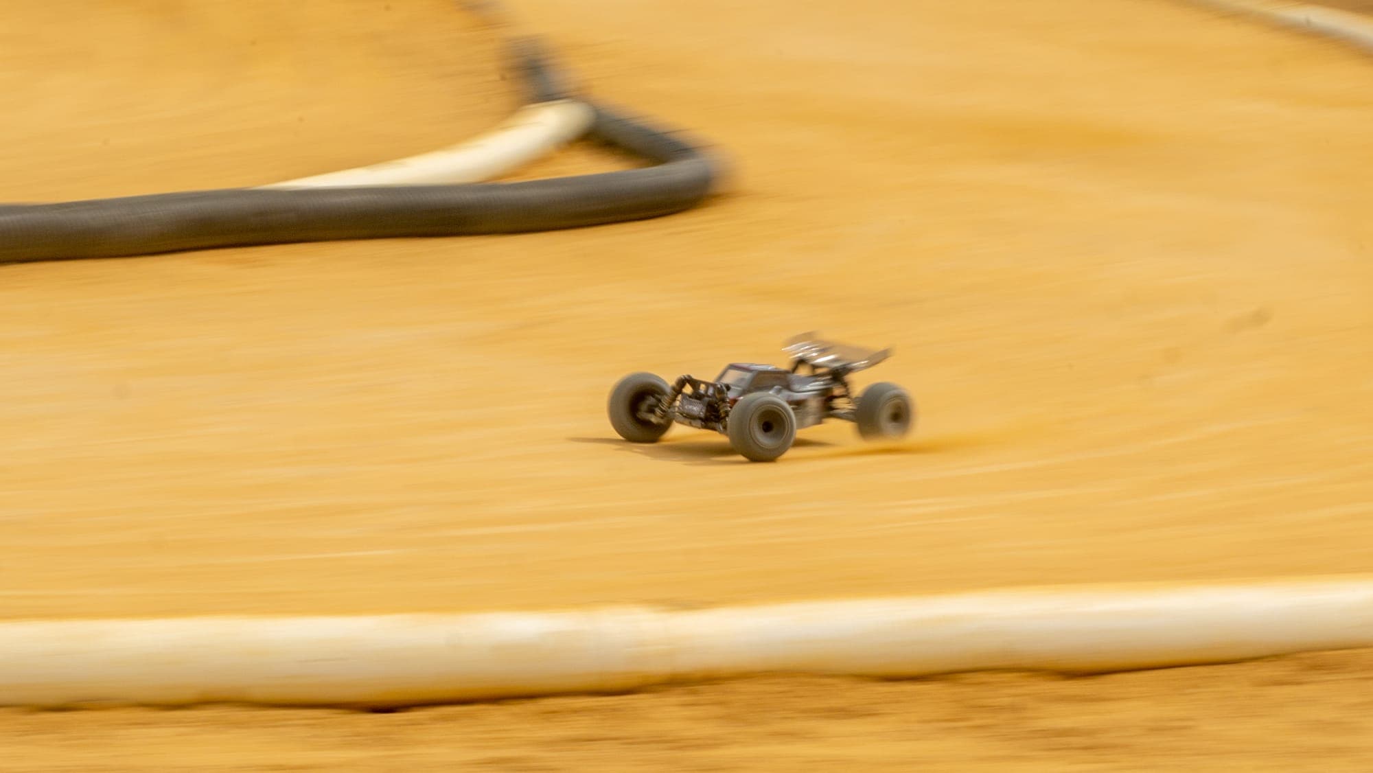 Radio-controlled buggy blurred mid-corner on a clay dirt track, panning motion streaking the ground.