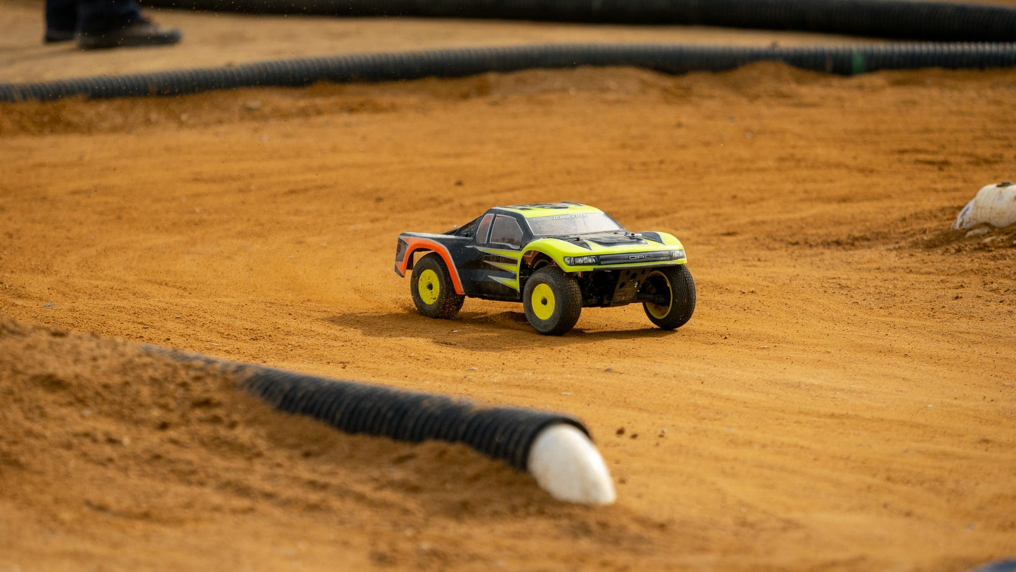 Yellow-and-black Losi short-course RC truck rolling through a dirt corner between track barriers.