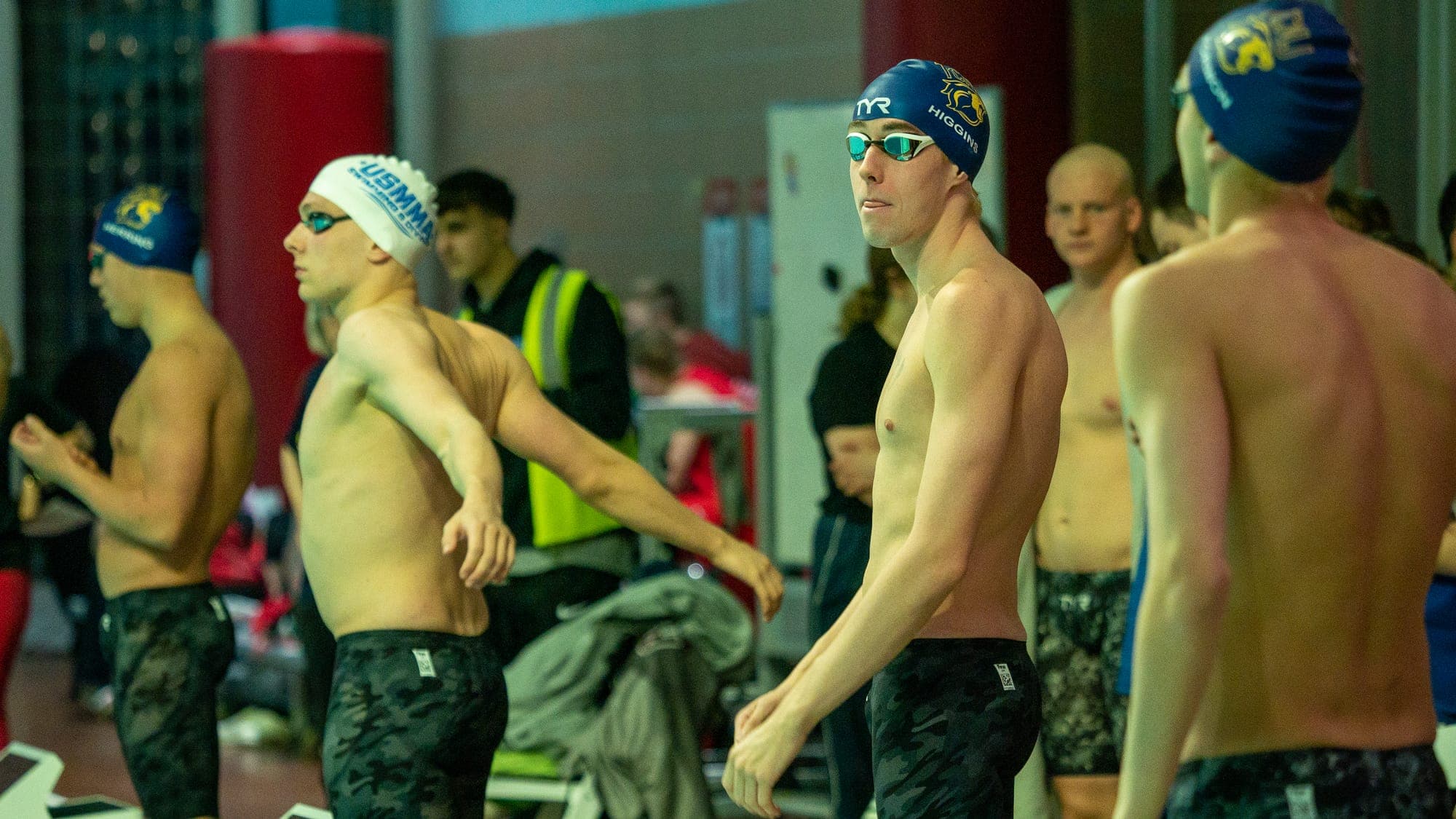 Swimmers in caps and goggles loosening up behind the blocks moments before their heat