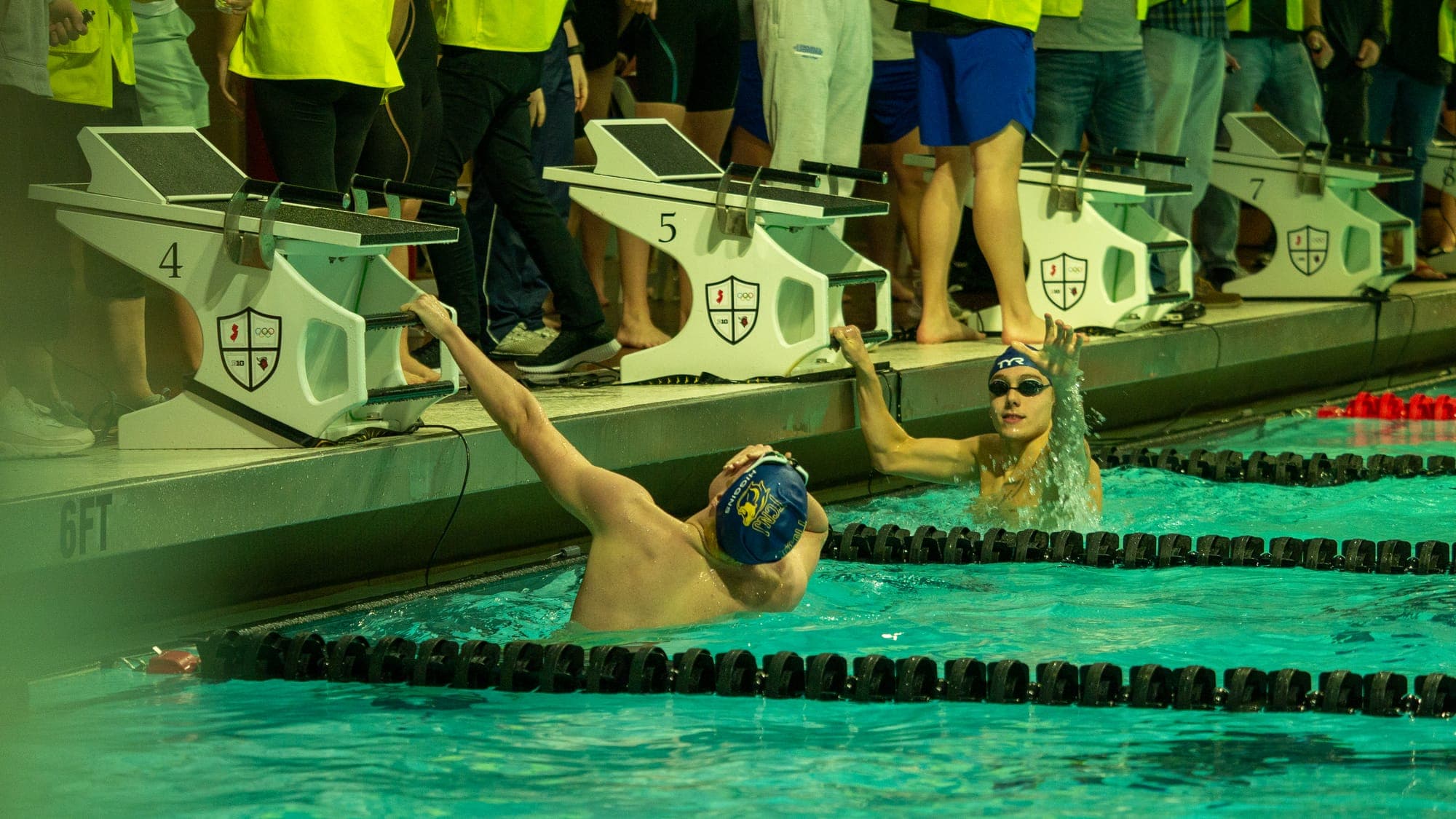 Two backstrokers gripping the starting blocks in lanes 4 and 5, coiled for the start signal