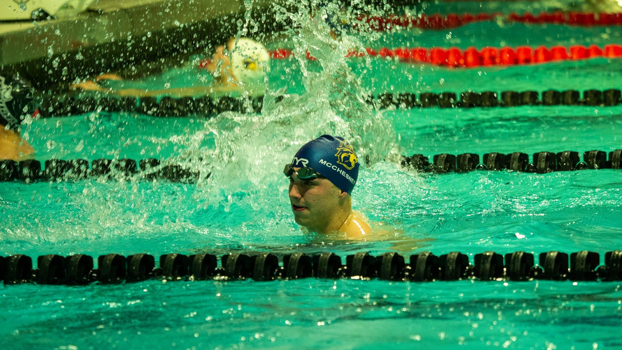 Swimmer in a blue cap lunging through the splash of his own stroke mid-race