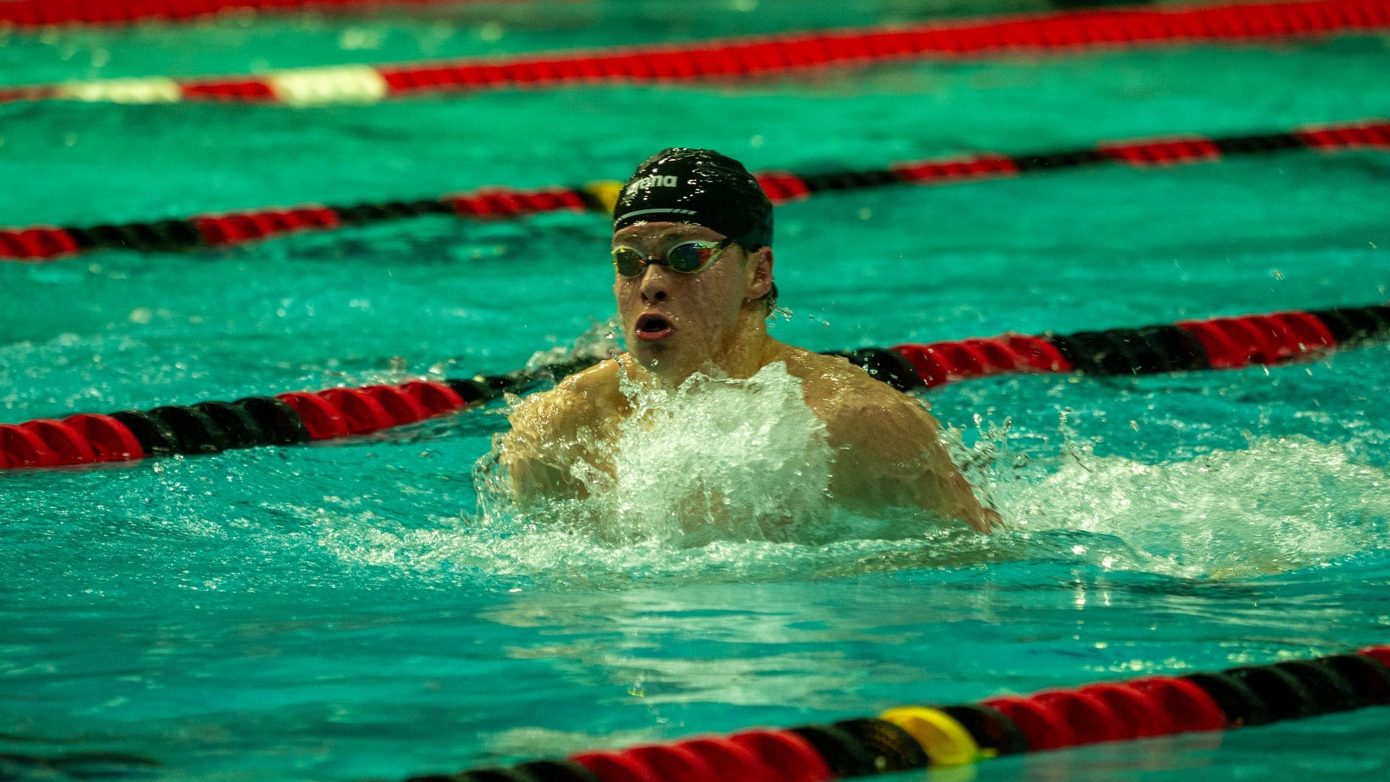 Breaststroker surging out of the water mid-stroke, mouth open for air as spray erupts around him