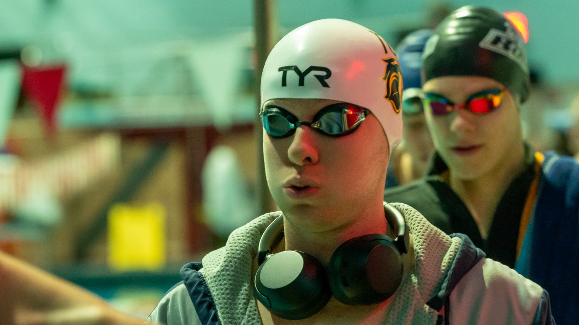 Swimmer in a white TYR cap with headphones around his neck, face lit by a streak of red light before his heat