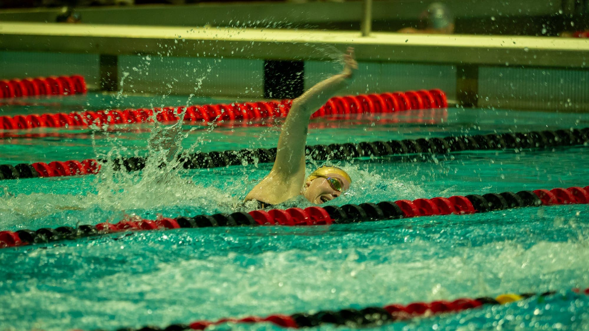Freestyler mid-stroke between red lane lines, arm arcing overhead through a curtain of spray