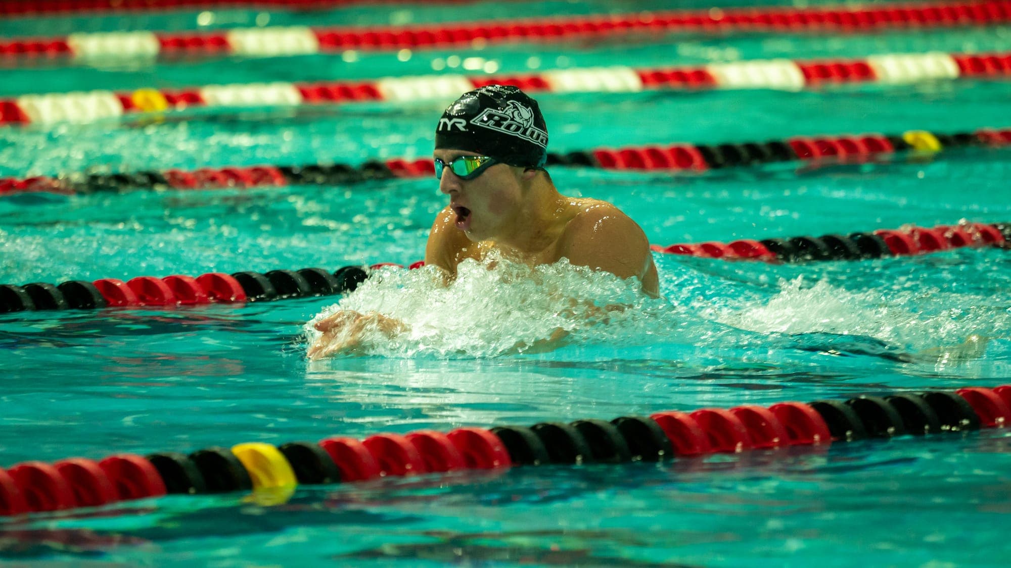 Breaststroke swimmer mid-pull, mouth open for air as water churns around his shoulders