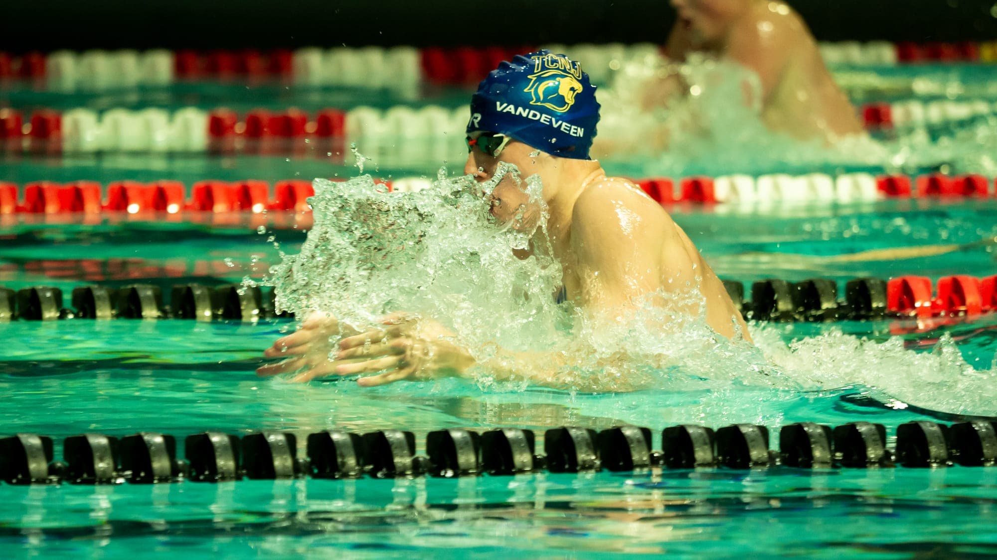 TCNJ breaststroke swimmer driving forward through a curtain of spray that veils his face