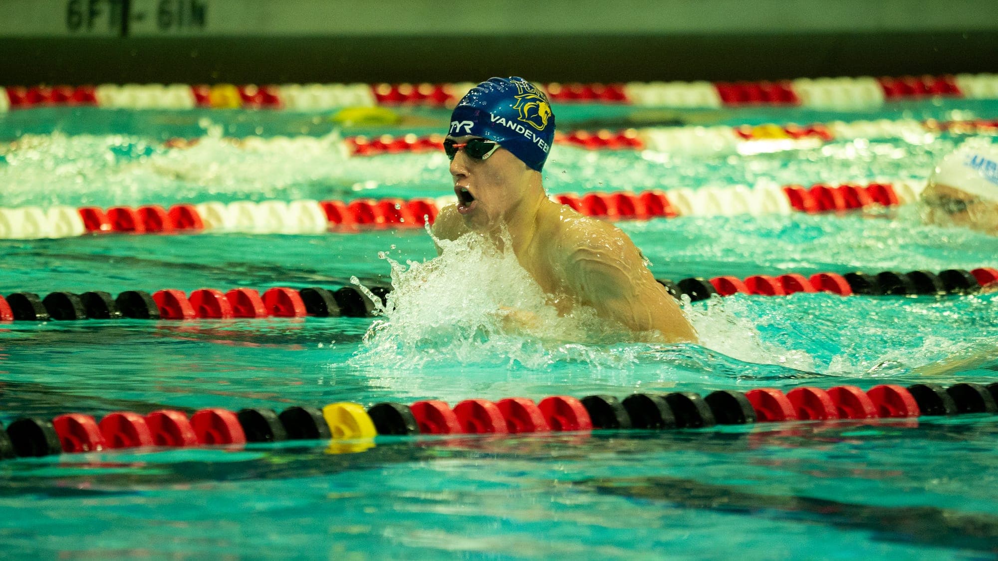 TCNJ breaststroke swimmer head-on at the top of his stroke, gasping for air above the wake