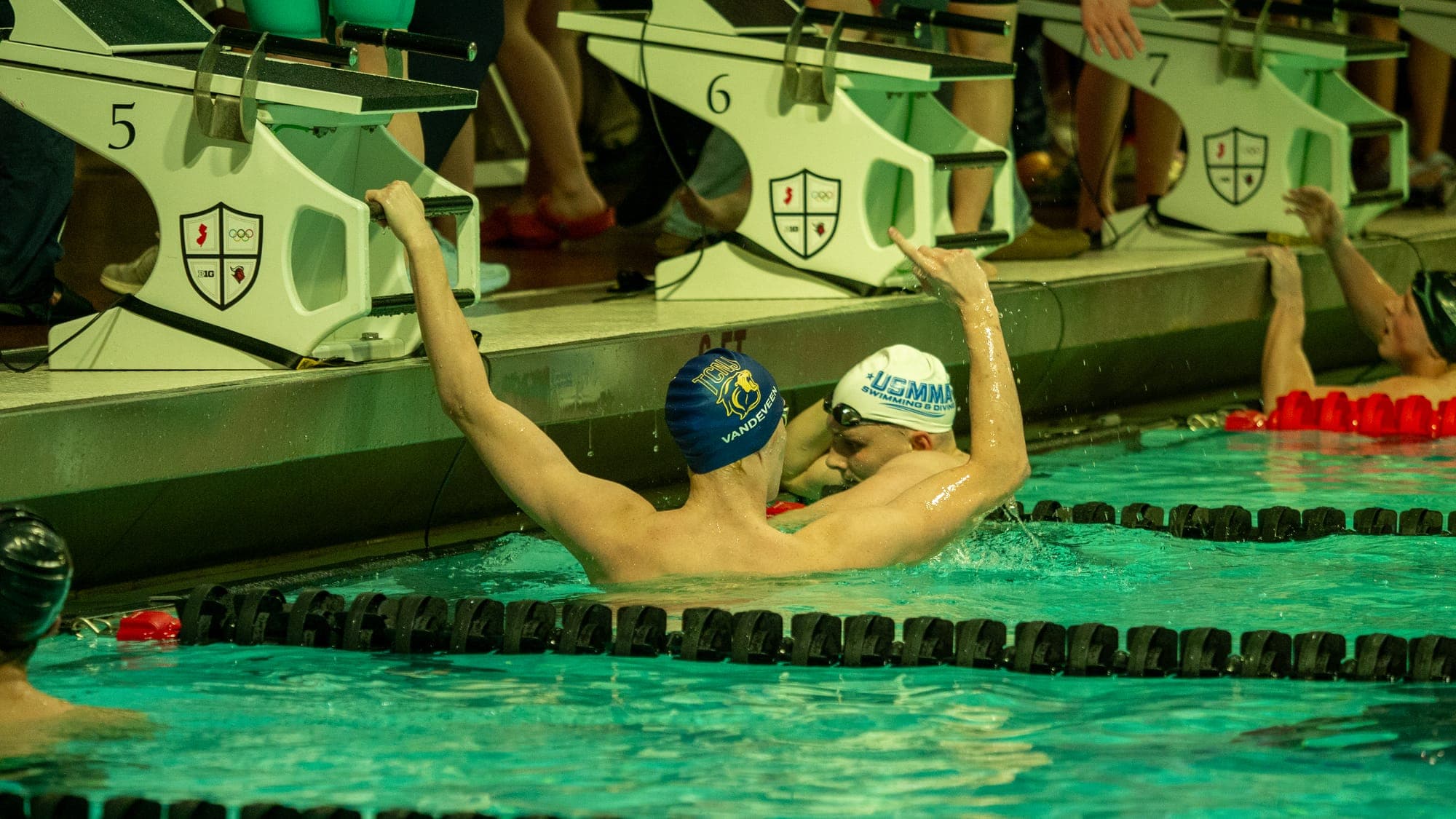 Swimmer raising a triumphant arm at the finish wall as the competitor in the next lane congratulates him
