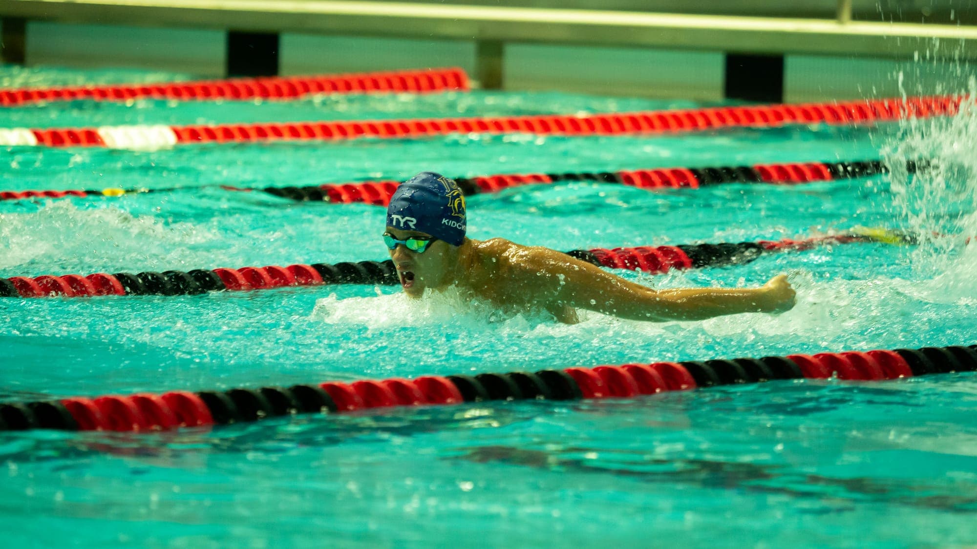 Butterfly swimmer lunging forward with arms outstretched over the churning water
