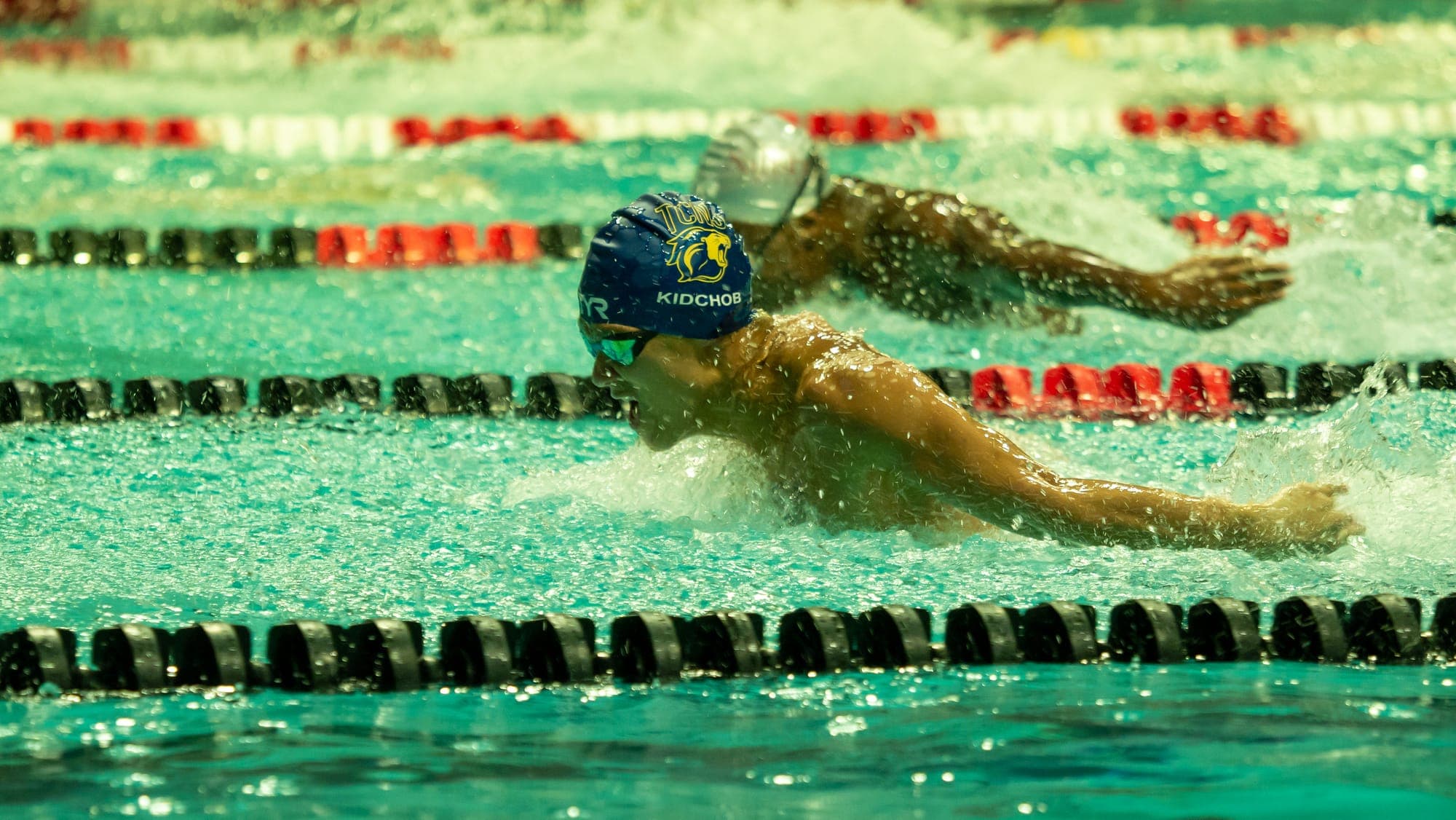 Two butterfly swimmers stroke for stroke in adjacent lanes, arms flung wide through the spray