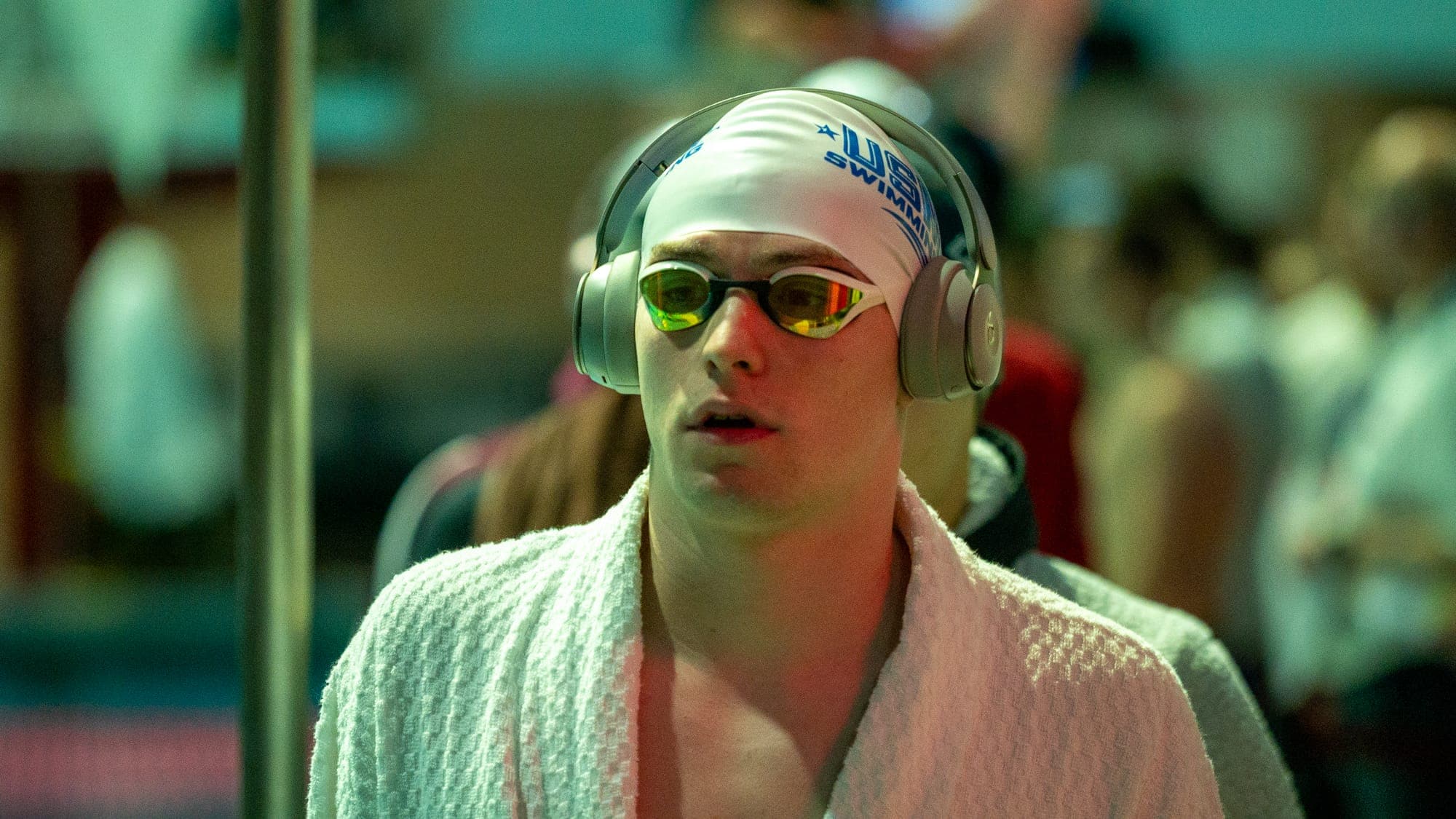 Swimmer in a USA Swimming cap and mirrored goggles wearing headphones and a white towel, locked in before a race