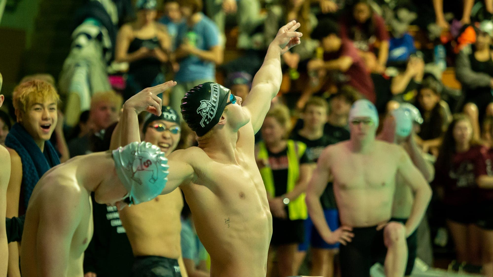 Swimmers swinging their arms to loosen up behind the starting blocks as packed bleachers look on