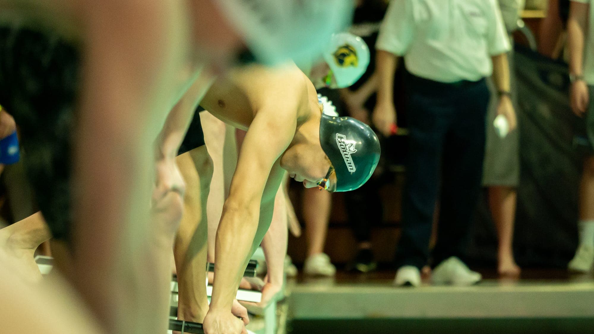 Swimmer in a Rowan cap coiled over the starting block, gripping its edge in the set position