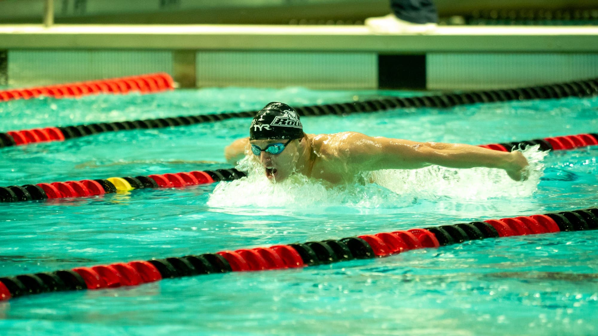 Butterfly swimmer lifting his head to breathe mid-stroke, water churning around outstretched arms