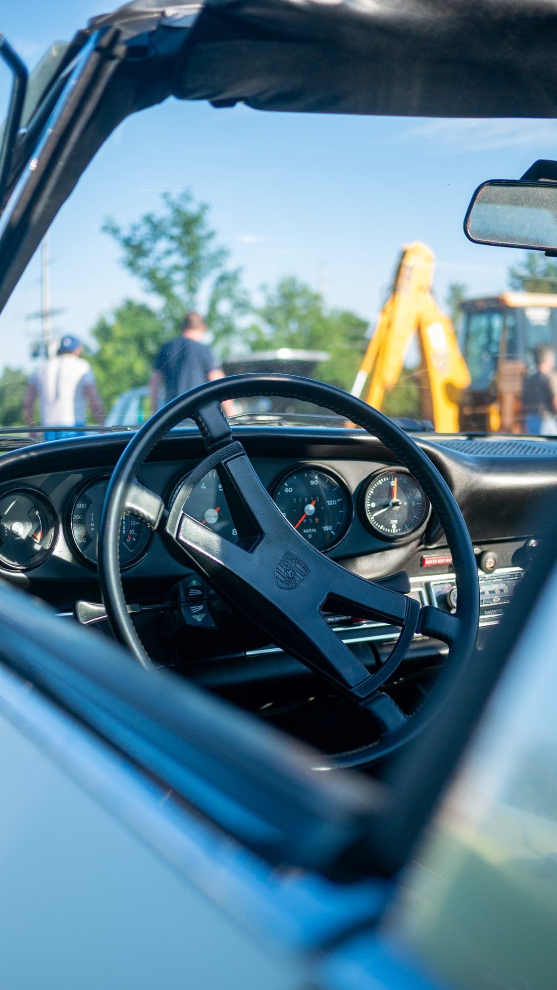 Classic Porsche 911 Targa cockpit seen through the open roof, black four-spoke wheel and gauges in morning sun.