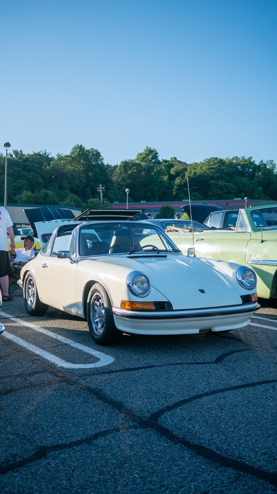 Ivory Porsche 911 Targa parked at a morning car show under a clear blue sky, chrome trim catching the low sun.