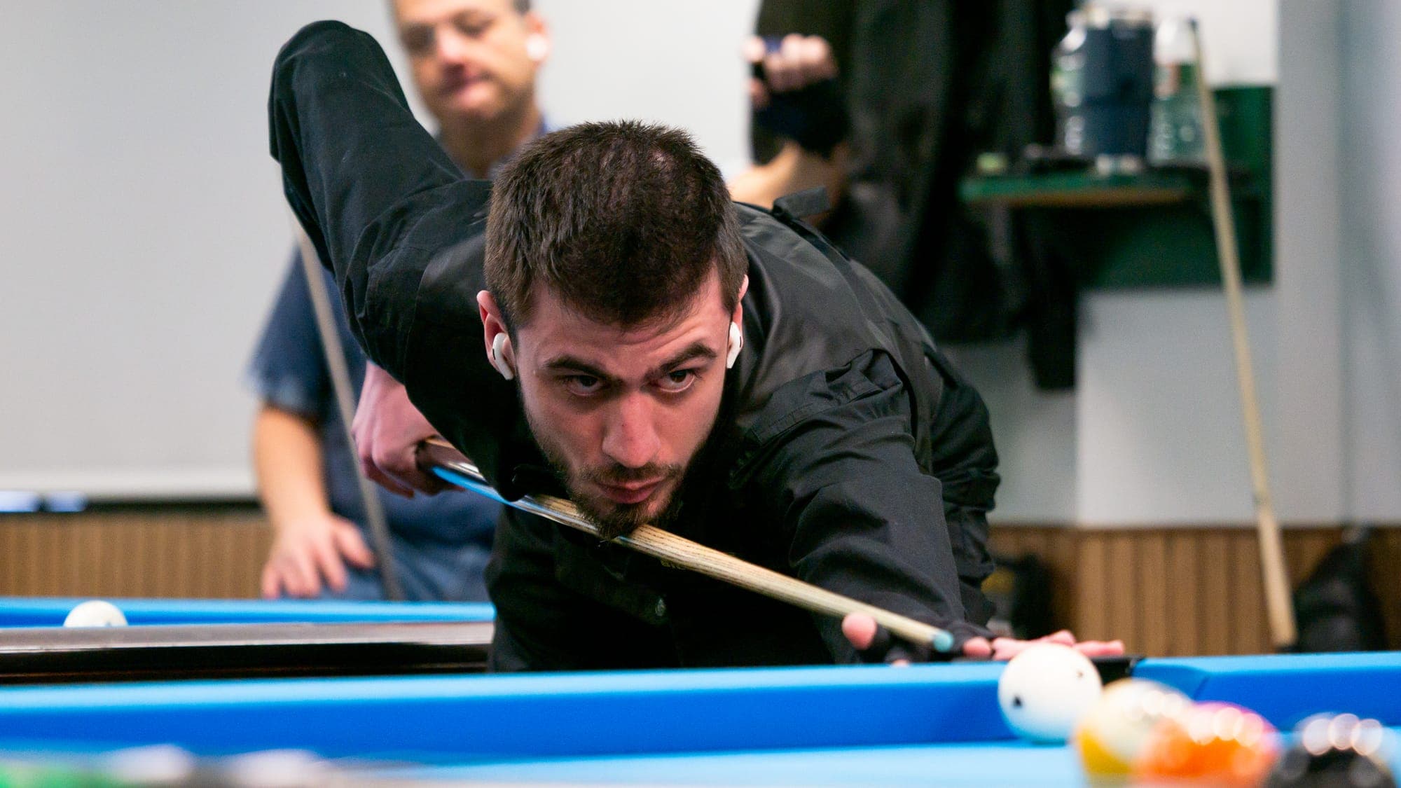 Billiards player in black leaning low over the cue, sighting down his shot across a blue-felt pool table