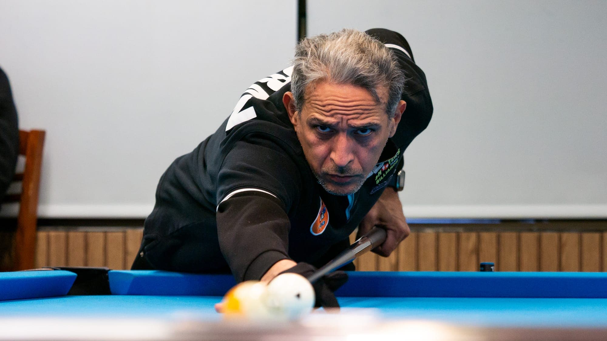 Gray-haired billiards player following through on a break, eyes locked over the blurred cue ball
