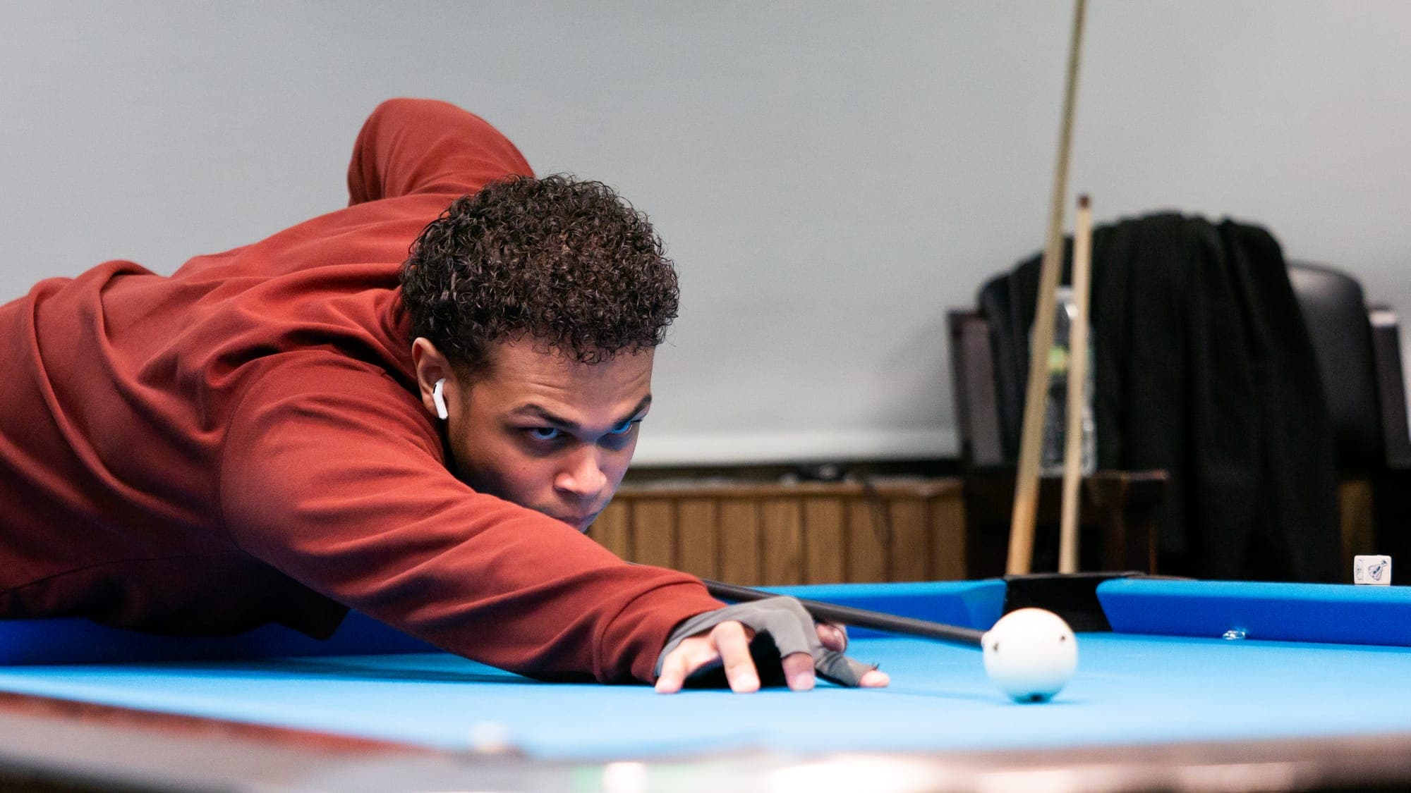 Billiards player in a maroon sweater sighting along his cue toward the cue ball at table level