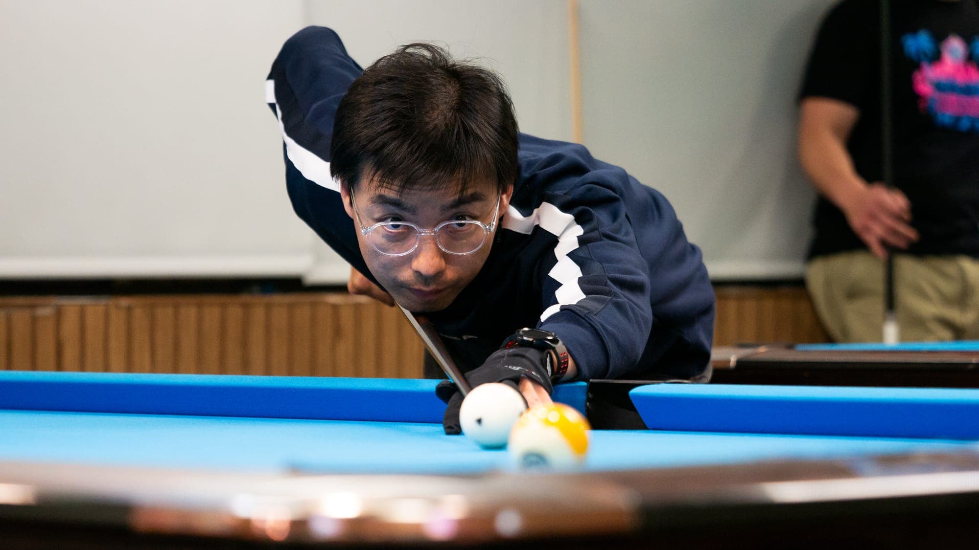 Bespectacled billiards player aiming down the cue at the white ball, brow furrowed in concentration