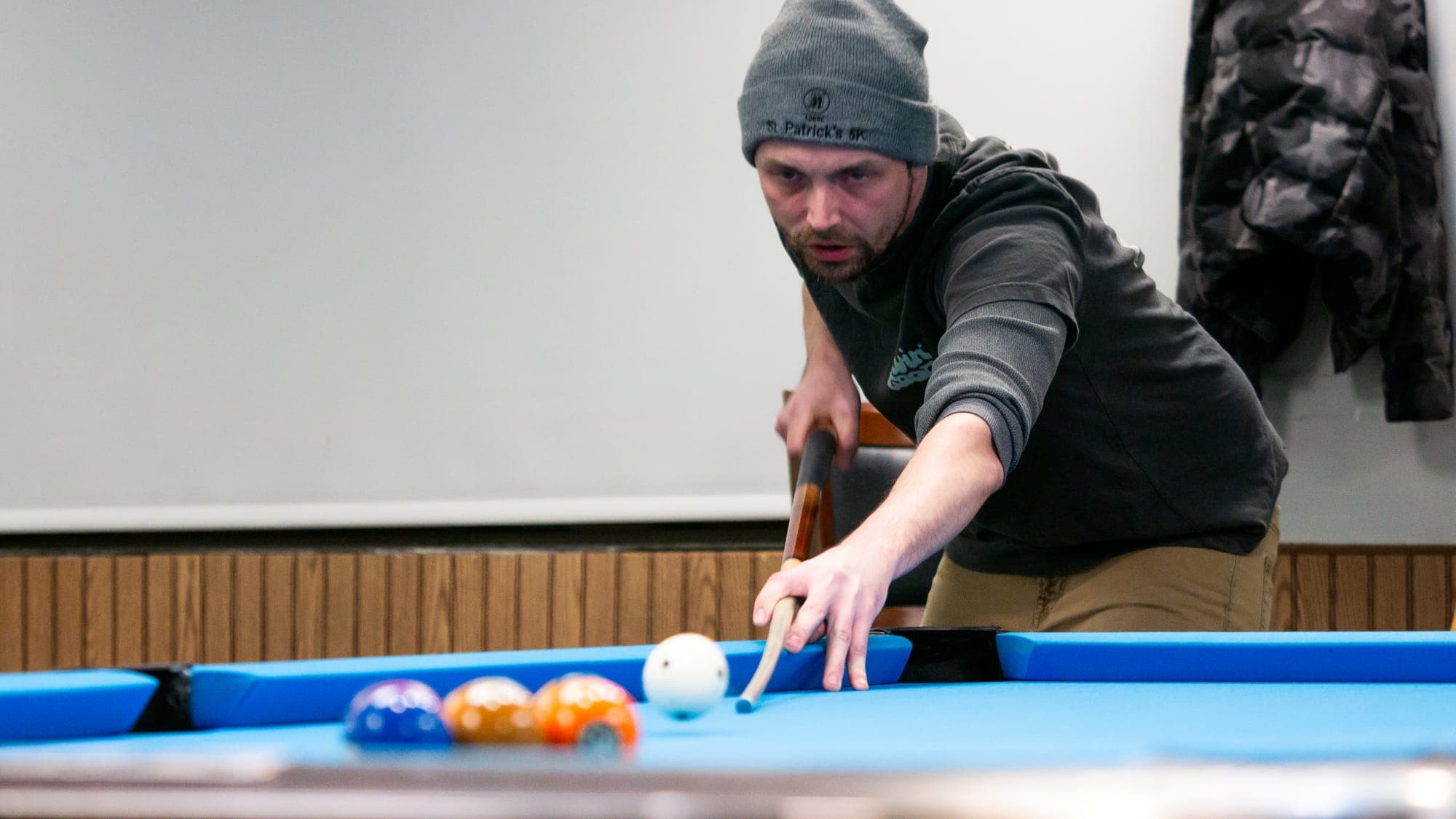 Pool player in a knit beanie reaching out to bridge a low shot beside the cue ball