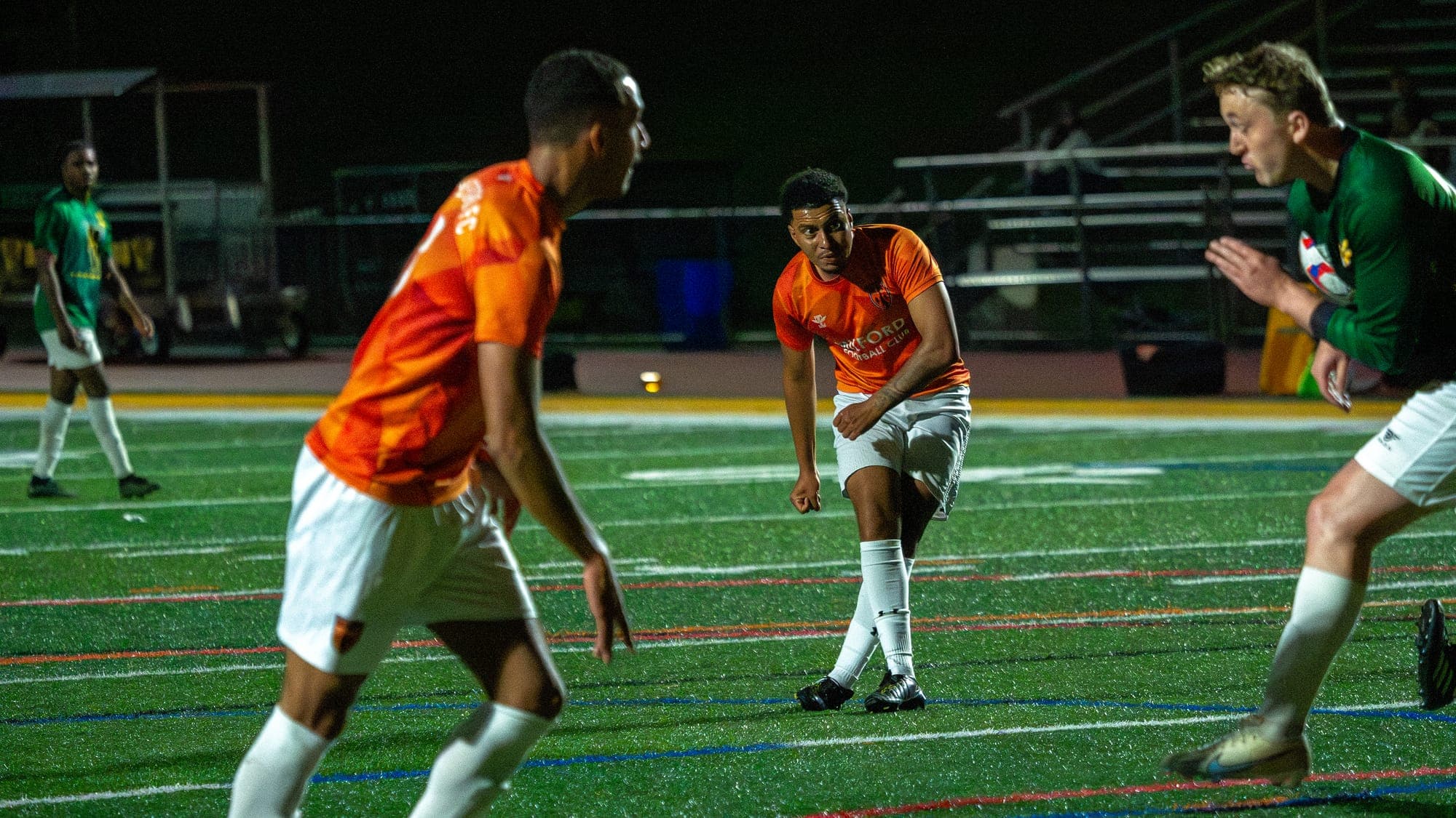 Soccer player following through on a pass under floodlights, framed between two other players