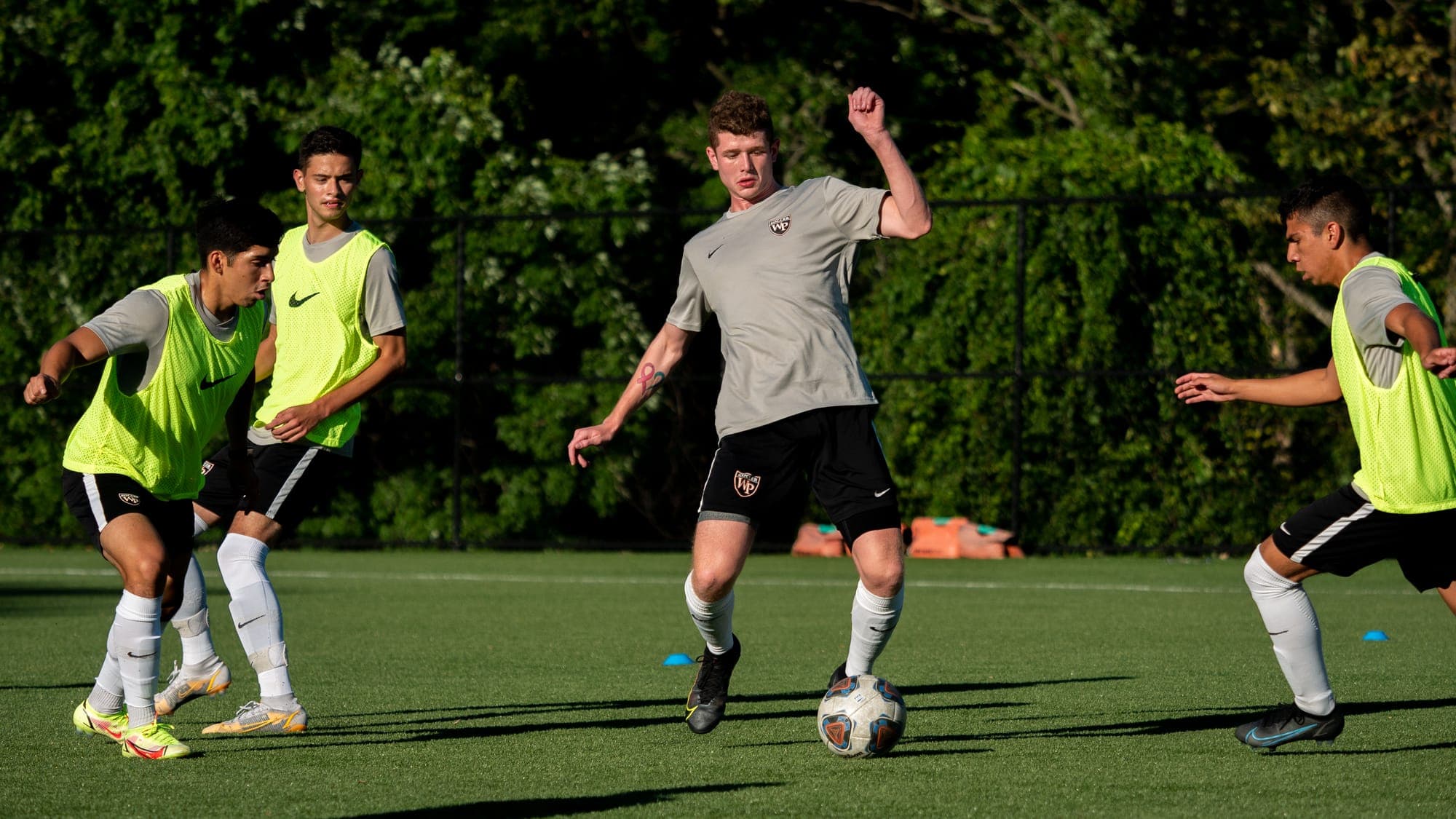 Soccer player in gray shielding the ball as three defenders in yellow bibs close in during a scrimmage