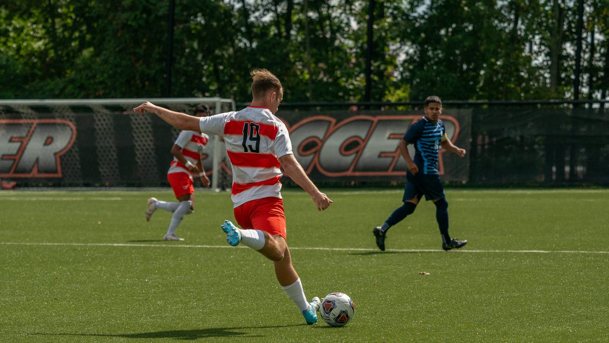 Soccer player number 19 winding up to strike the ball with his right foot in open play