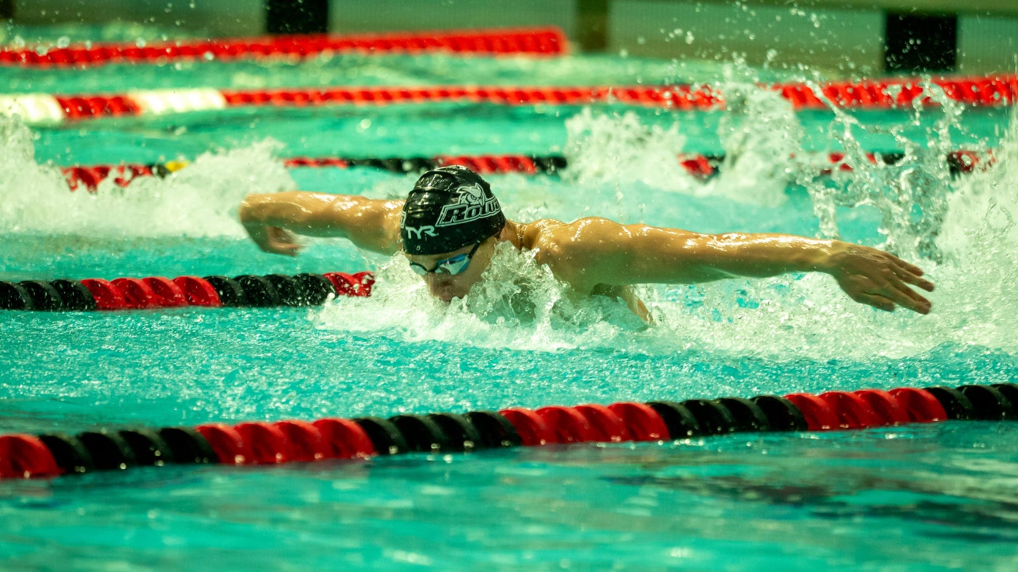 Butterfly swimmer surging through red lane lines, arms swept wide in a burst of spray