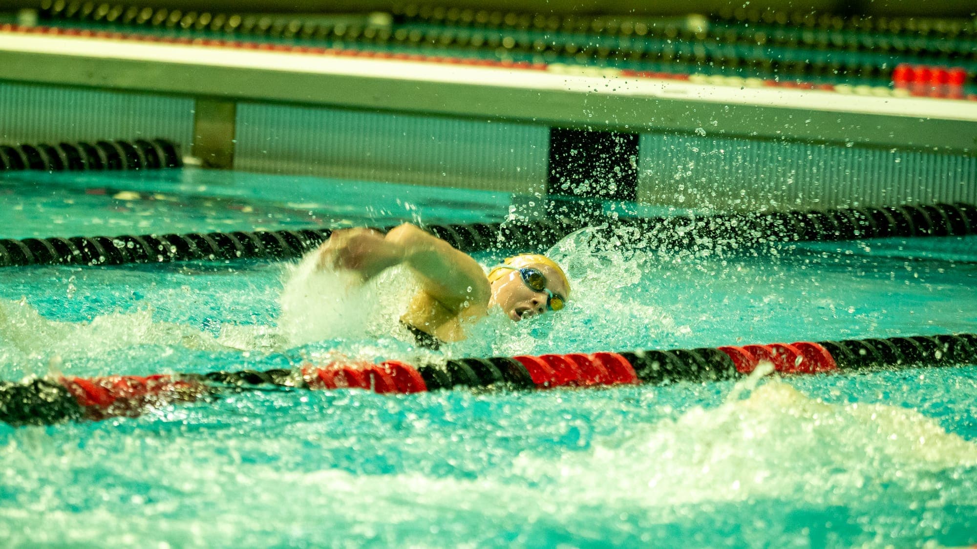 Freestyle swimmer turning to breathe mid-stroke, droplets frozen above the lane line